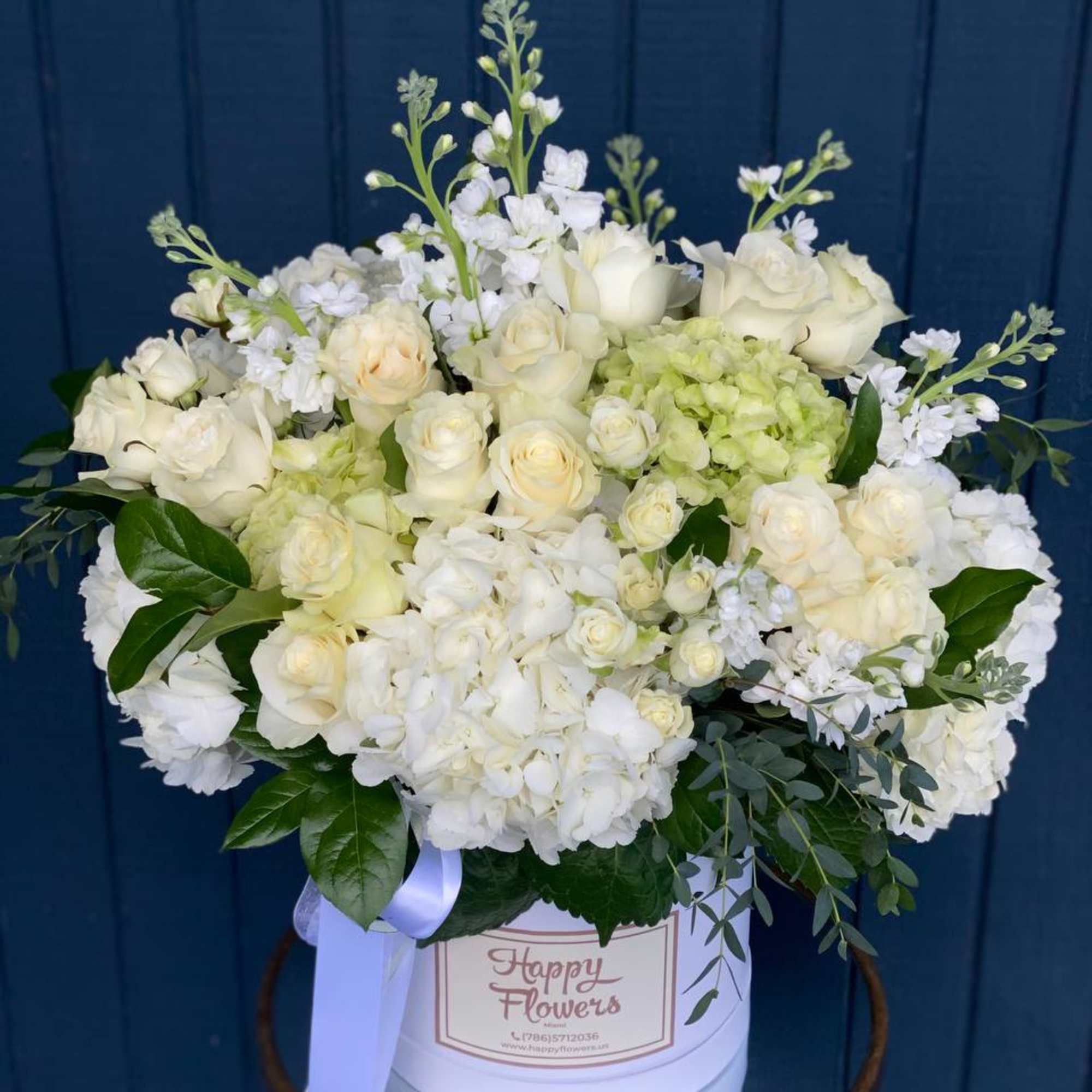 White roses and hydrangeas arranged in a round hatbox with a ribbon