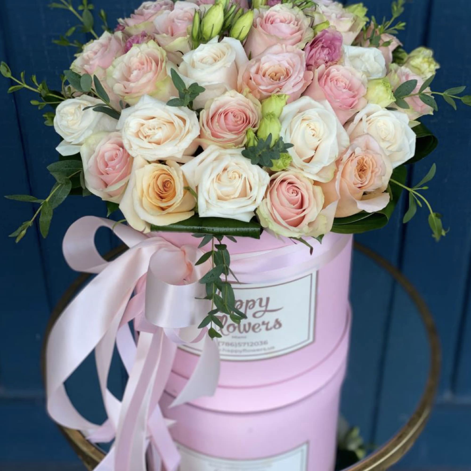 Pink and white roses arranged in a pink hat box with a ribbon.