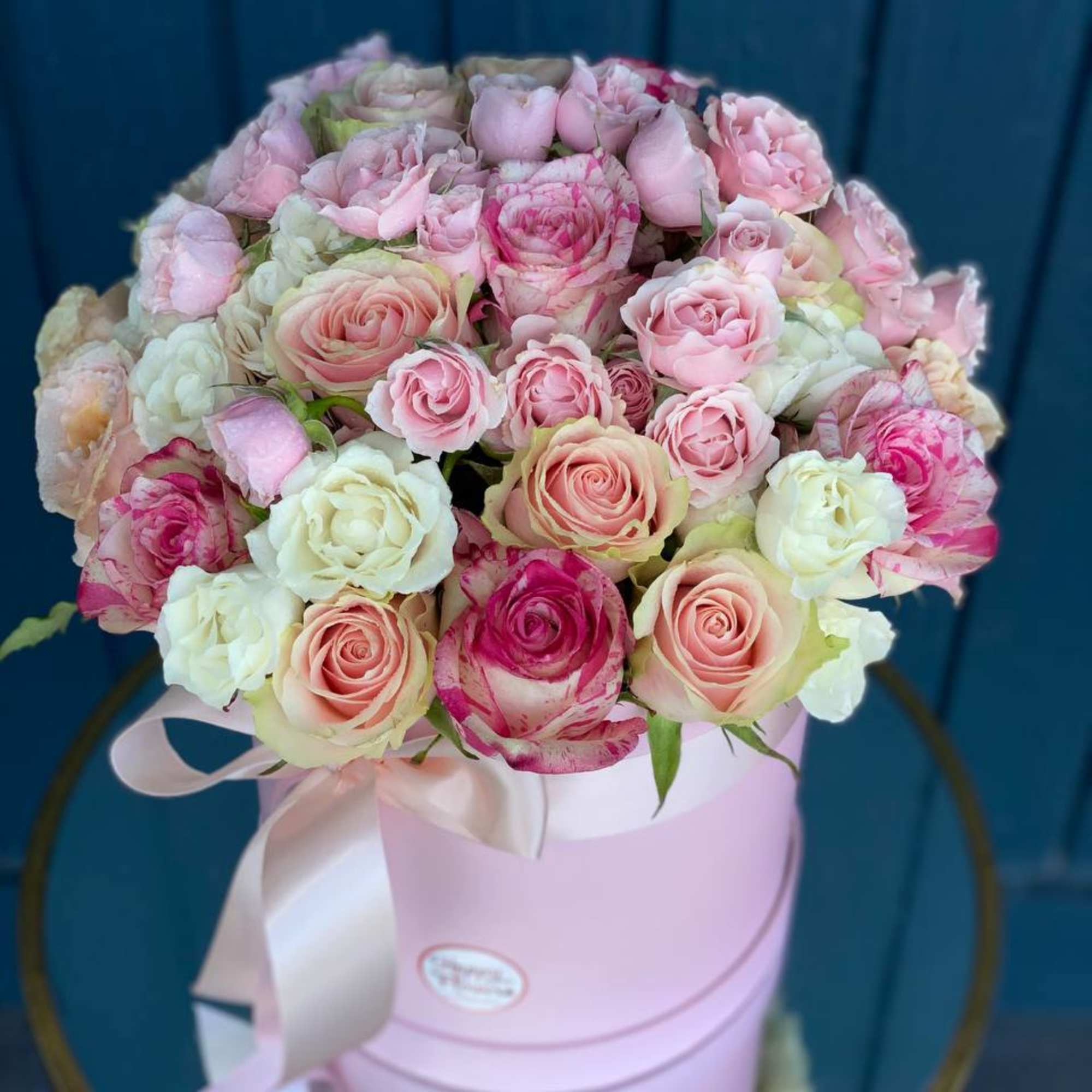 Pink and white roses arranged in a pastel pink hat box with ribbon