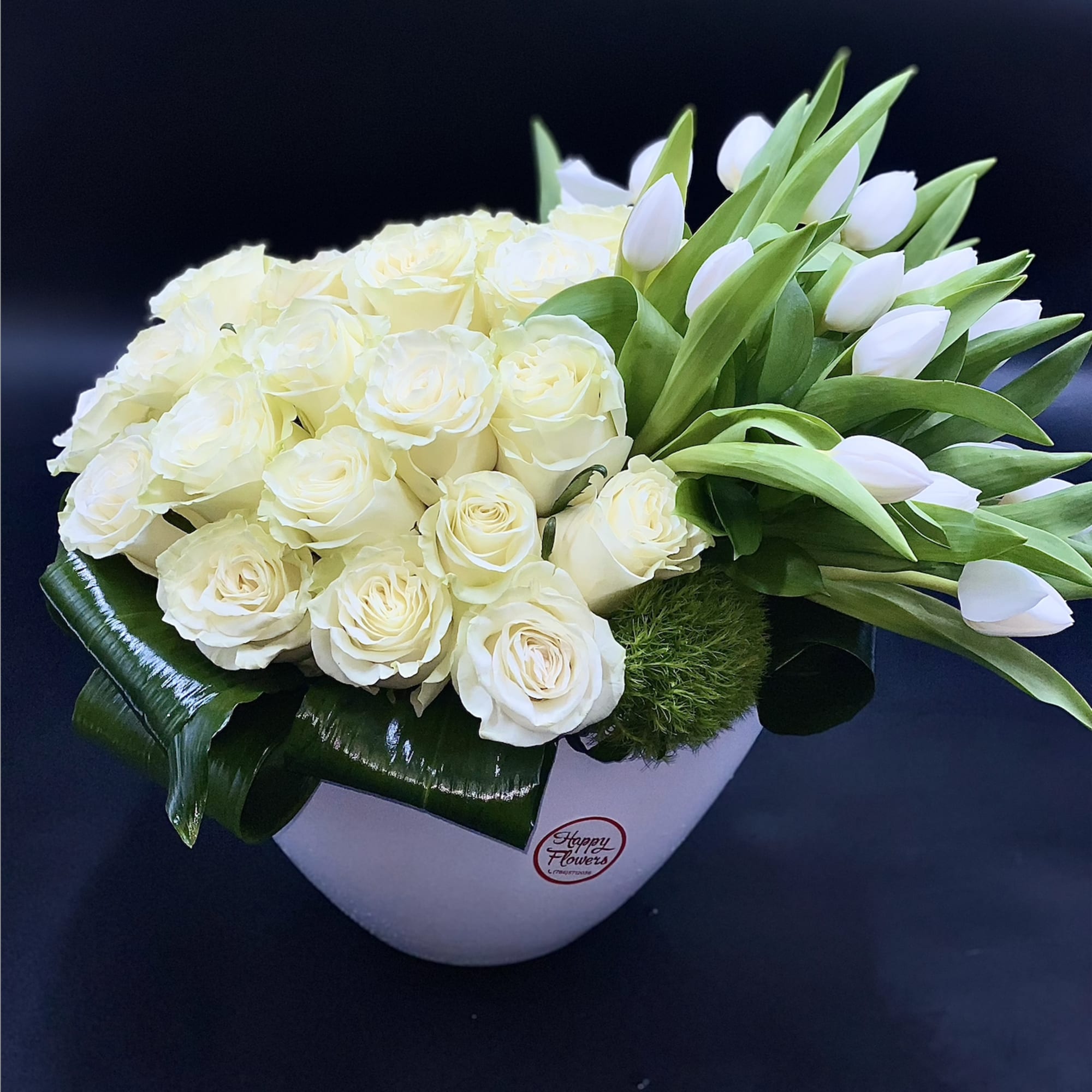 White roses and tulips arranged in a white heart-shaped box