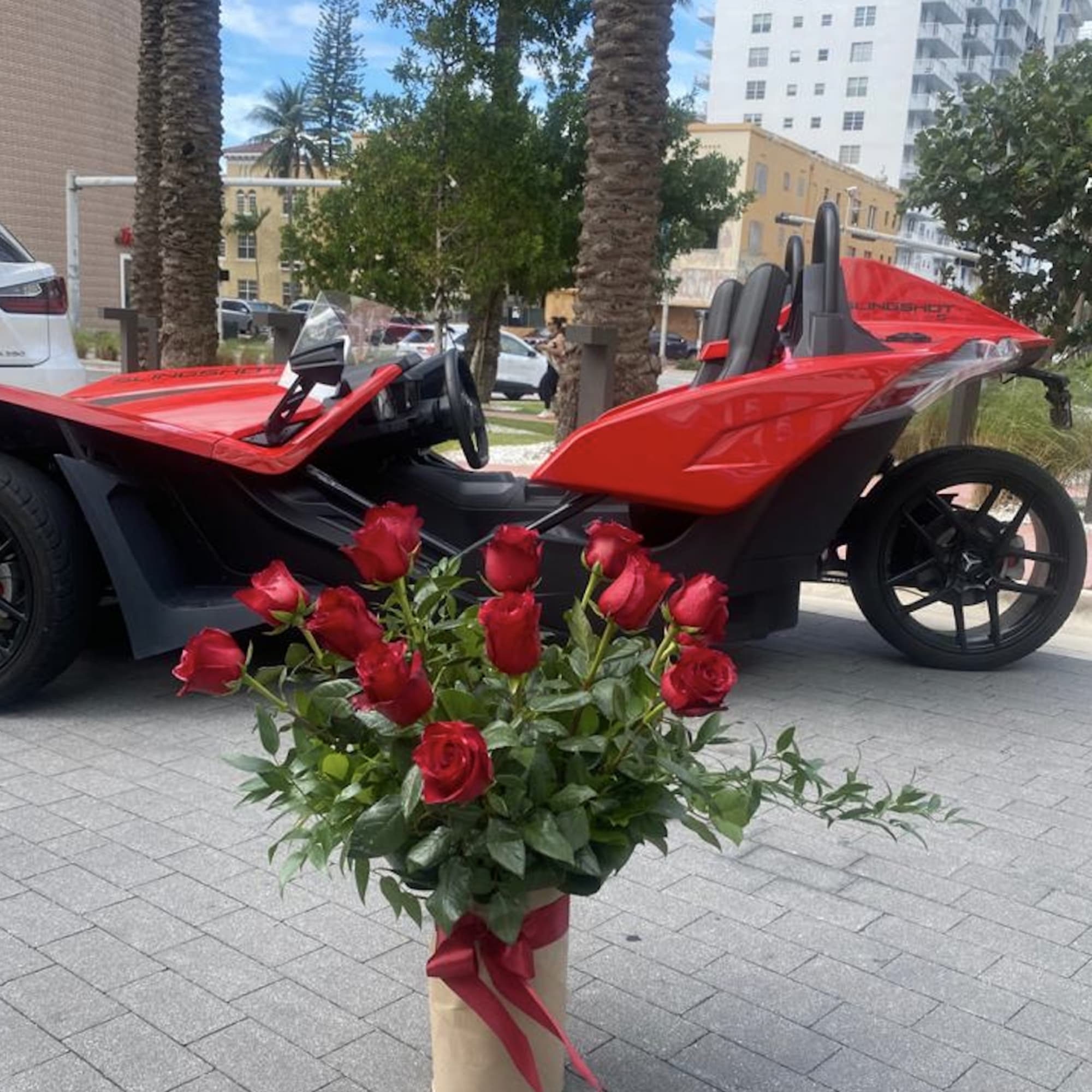 Red roses arranged in a wrapped bouquet in front of a red three-wheeled vehicle