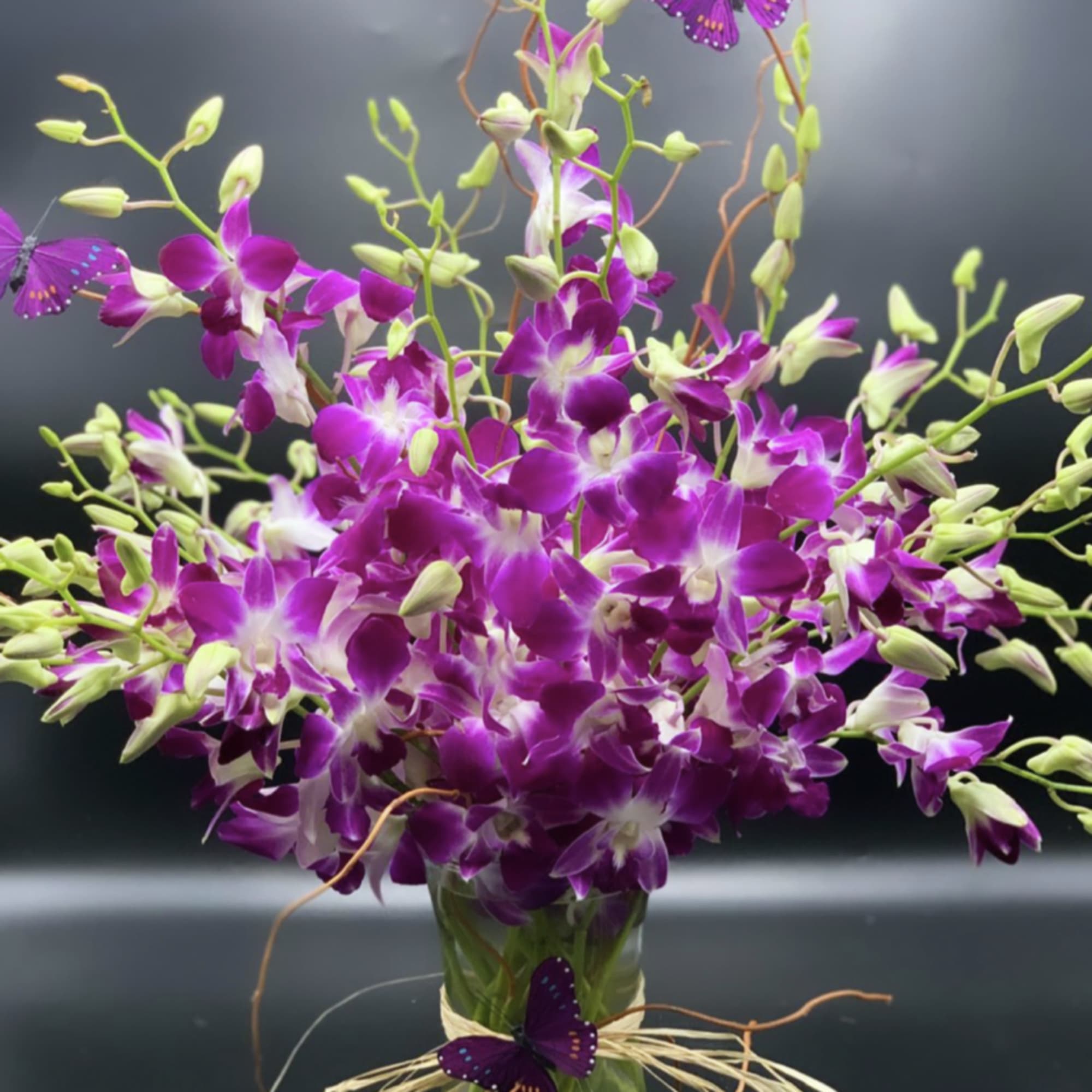Purple orchids in a glass vase with decorative butterflies