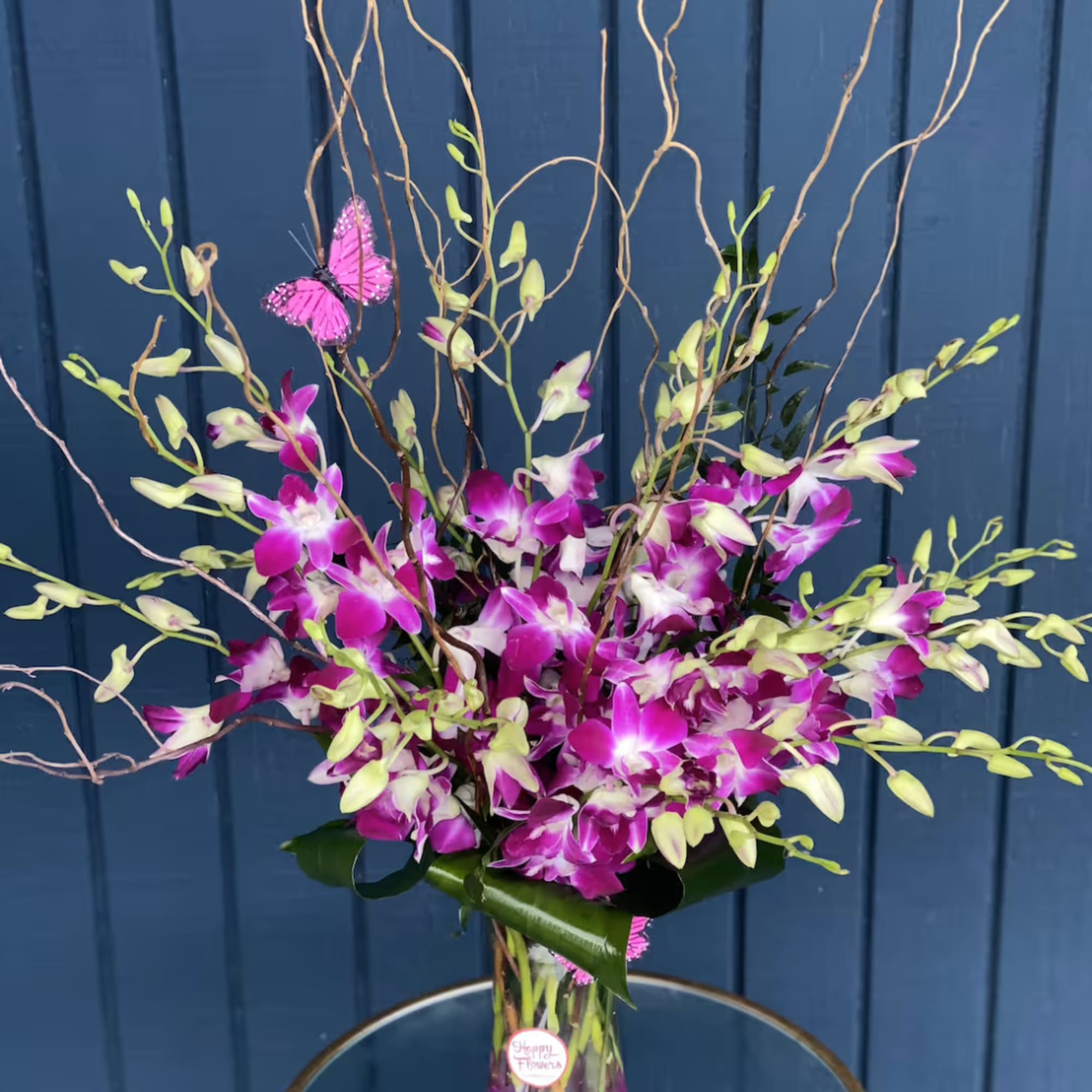Tall orchid arrangement in a clear vase with pink butterflies
