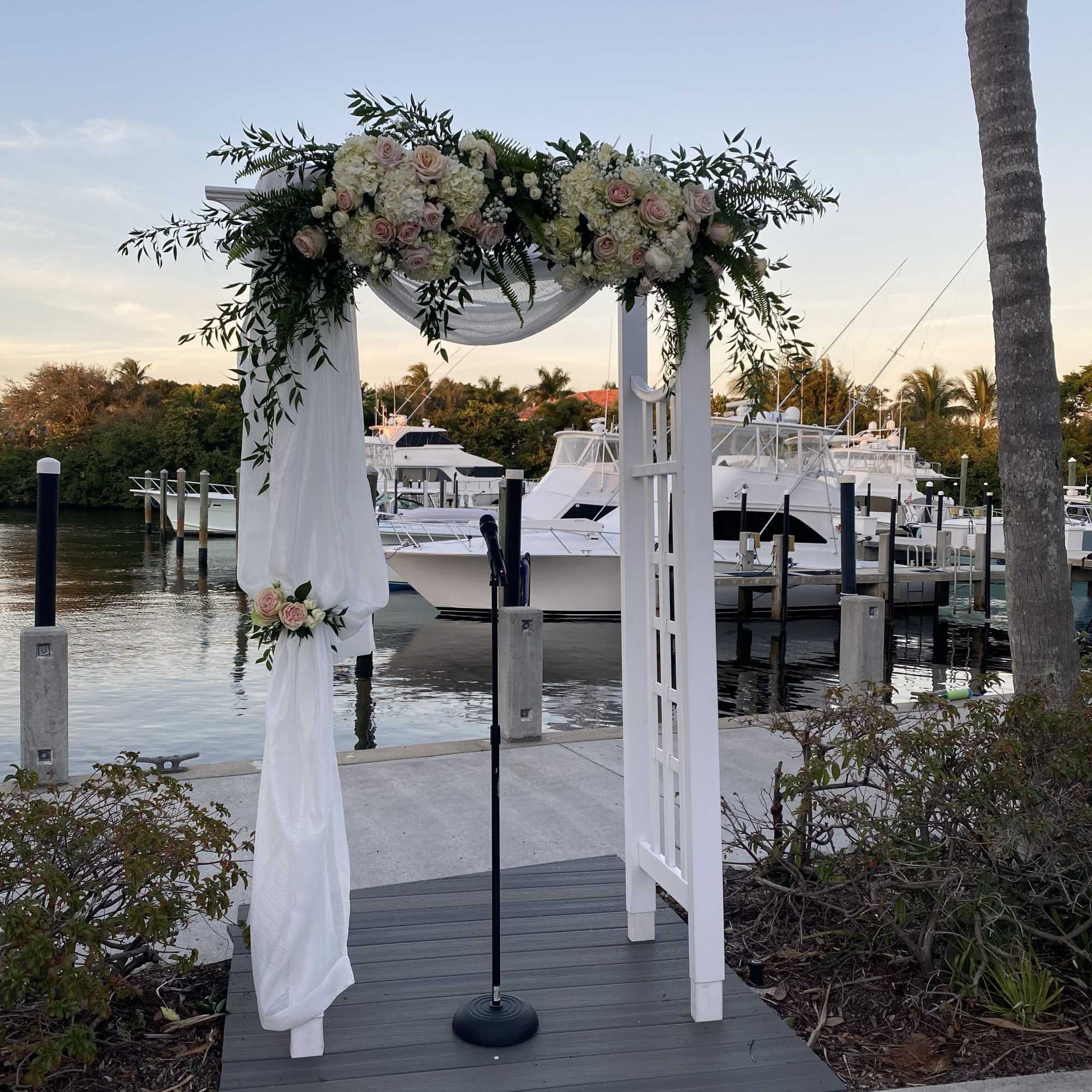 White floral arch with pink roses and draped fabric by a marina