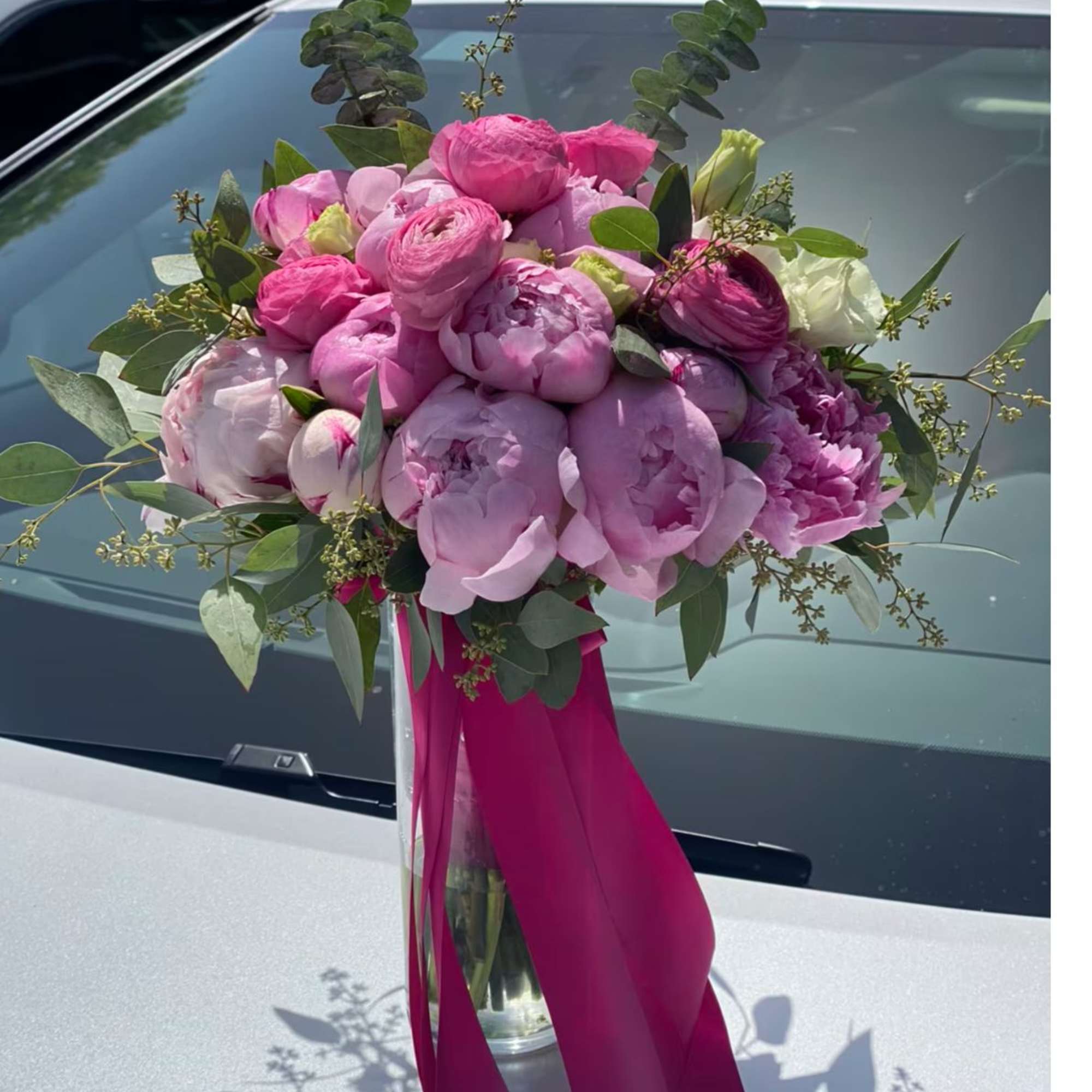 Pink peony bouquet in a glass vase with a magenta ribbon