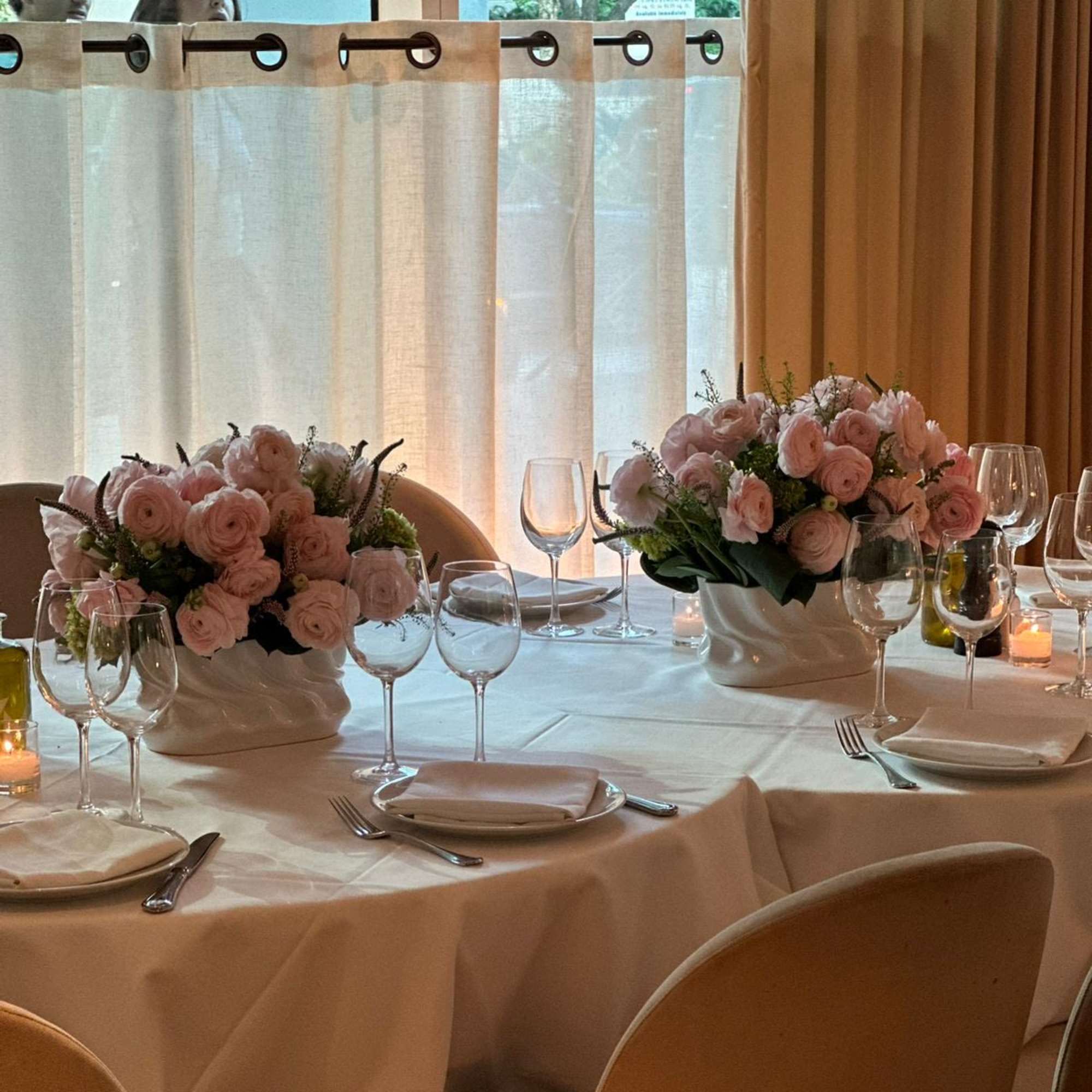 Pink rose centerpieces in white ceramic bowls on a set dining table