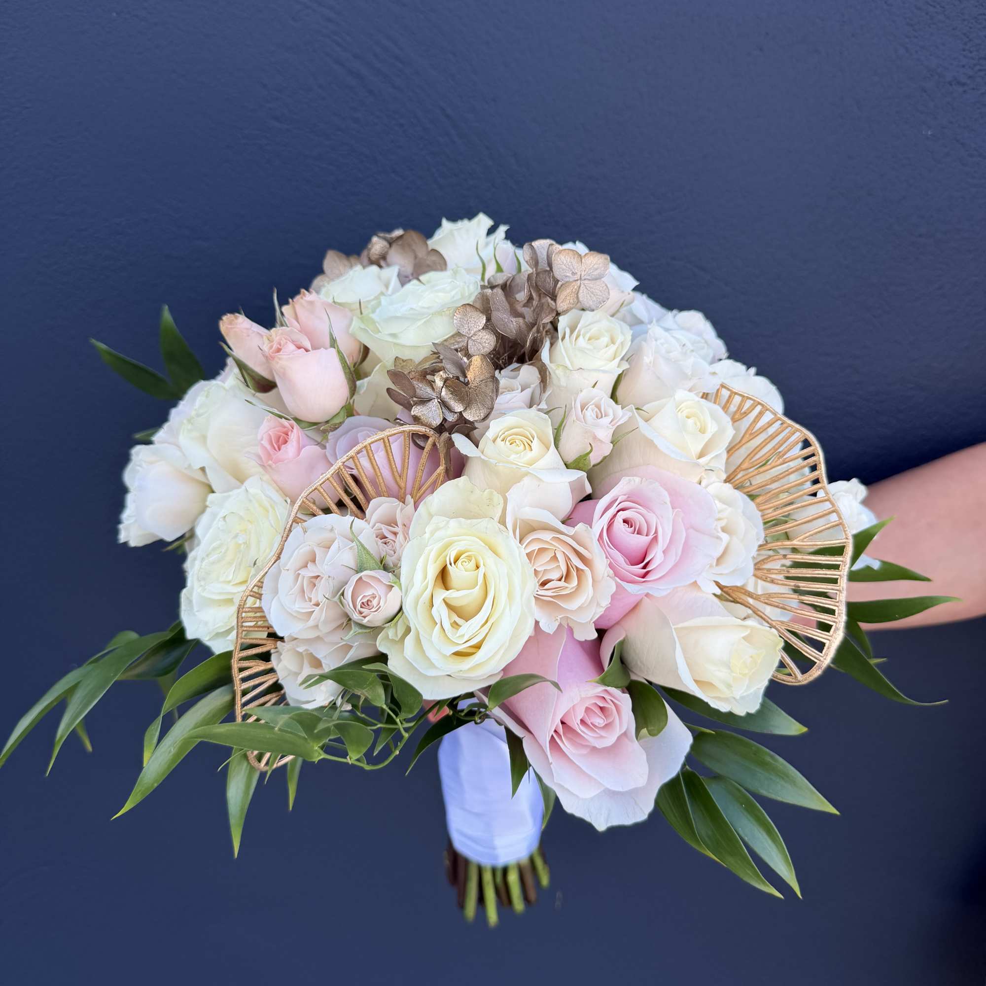 Handheld bouquet of pale pink and white roses with gold decorative accents