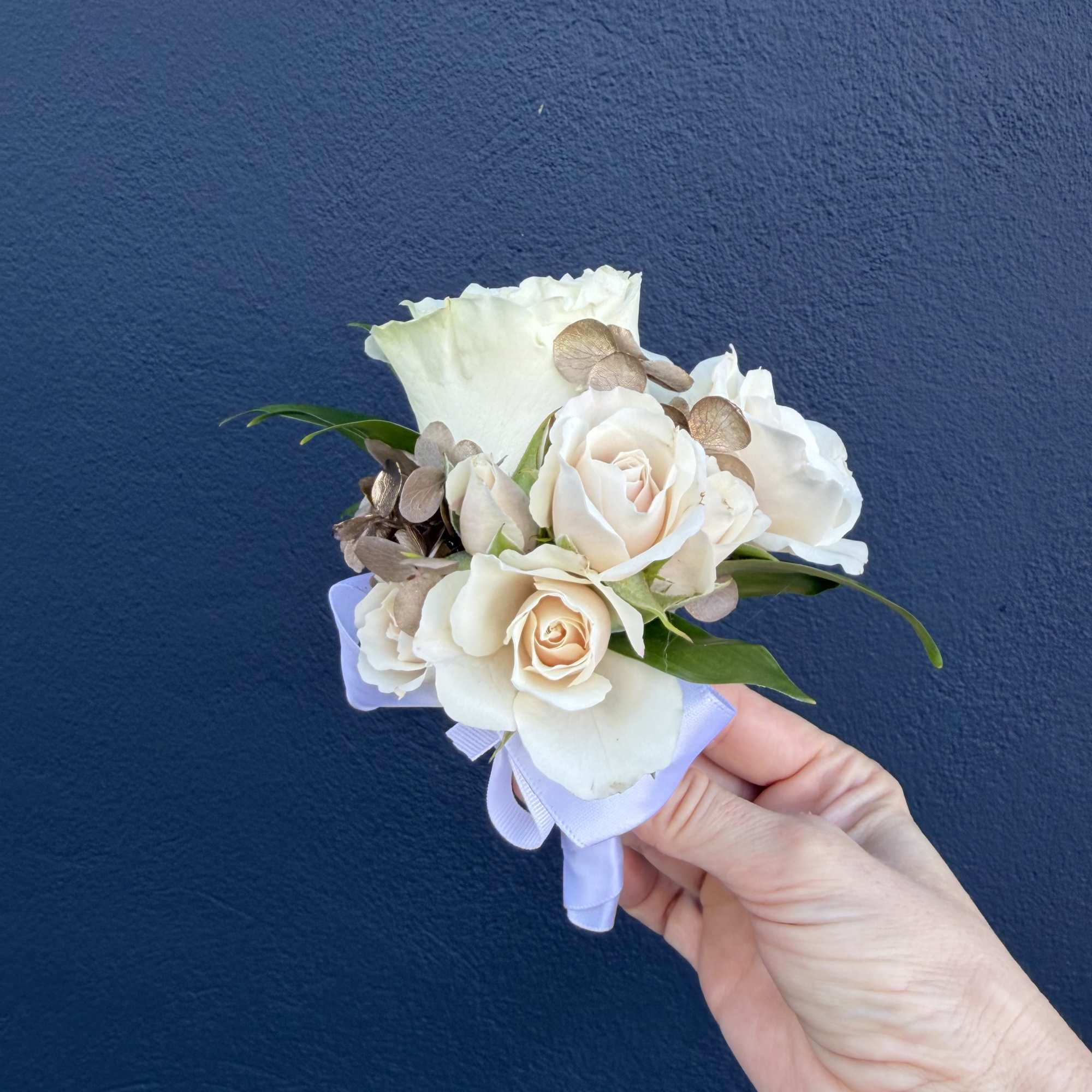 Small white rose boutonniere with ribbon and greenery held in a hand