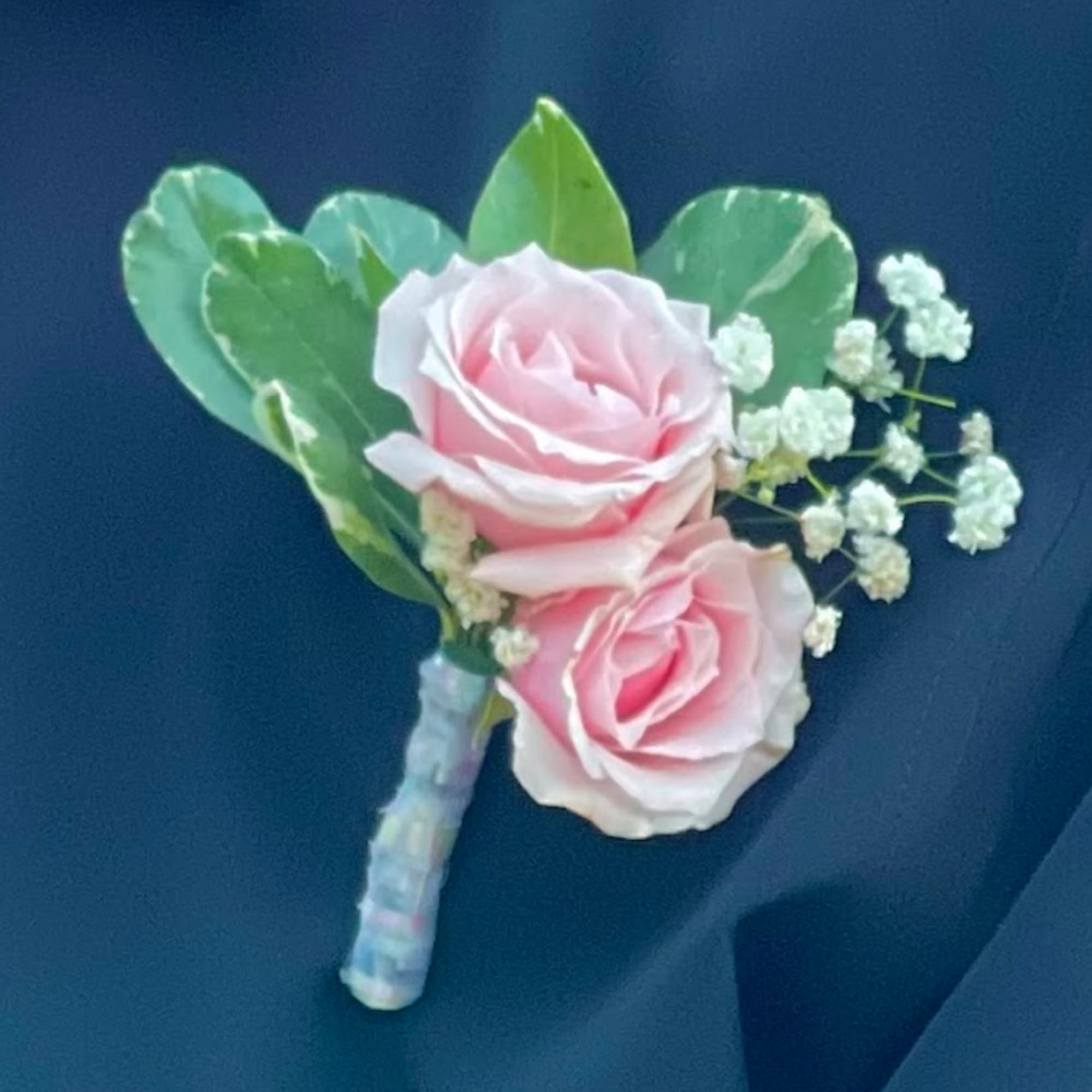Pink rose boutonniere with baby's breath and green leaves