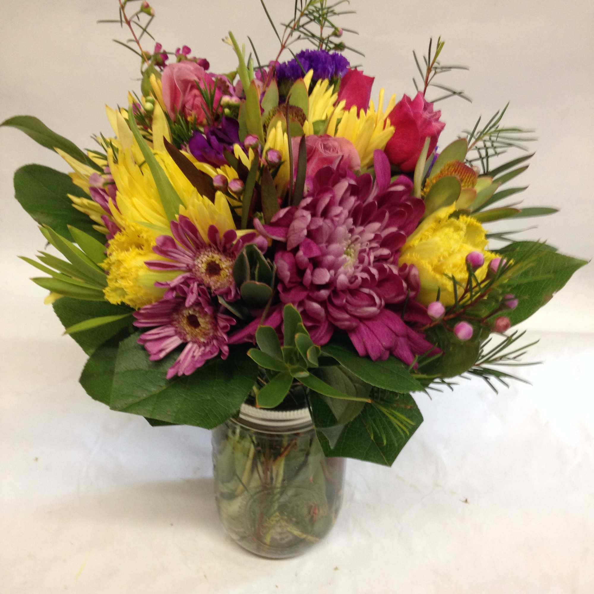 Mixed bouquet of pink, yellow, and purple flowers in a glass jar vase
