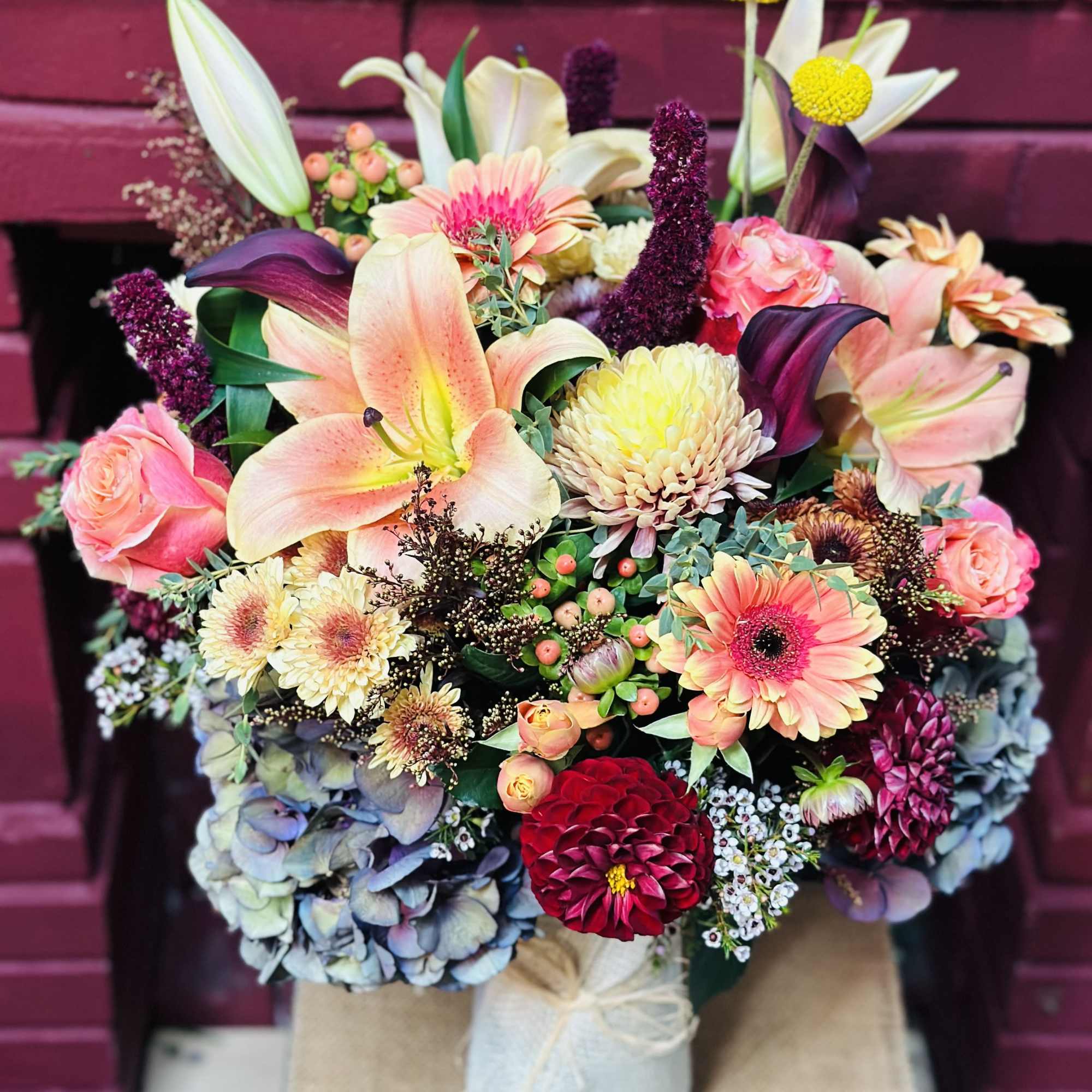 Mixed bouquet with lilies, roses, and gerbera daisies in a wrapped container