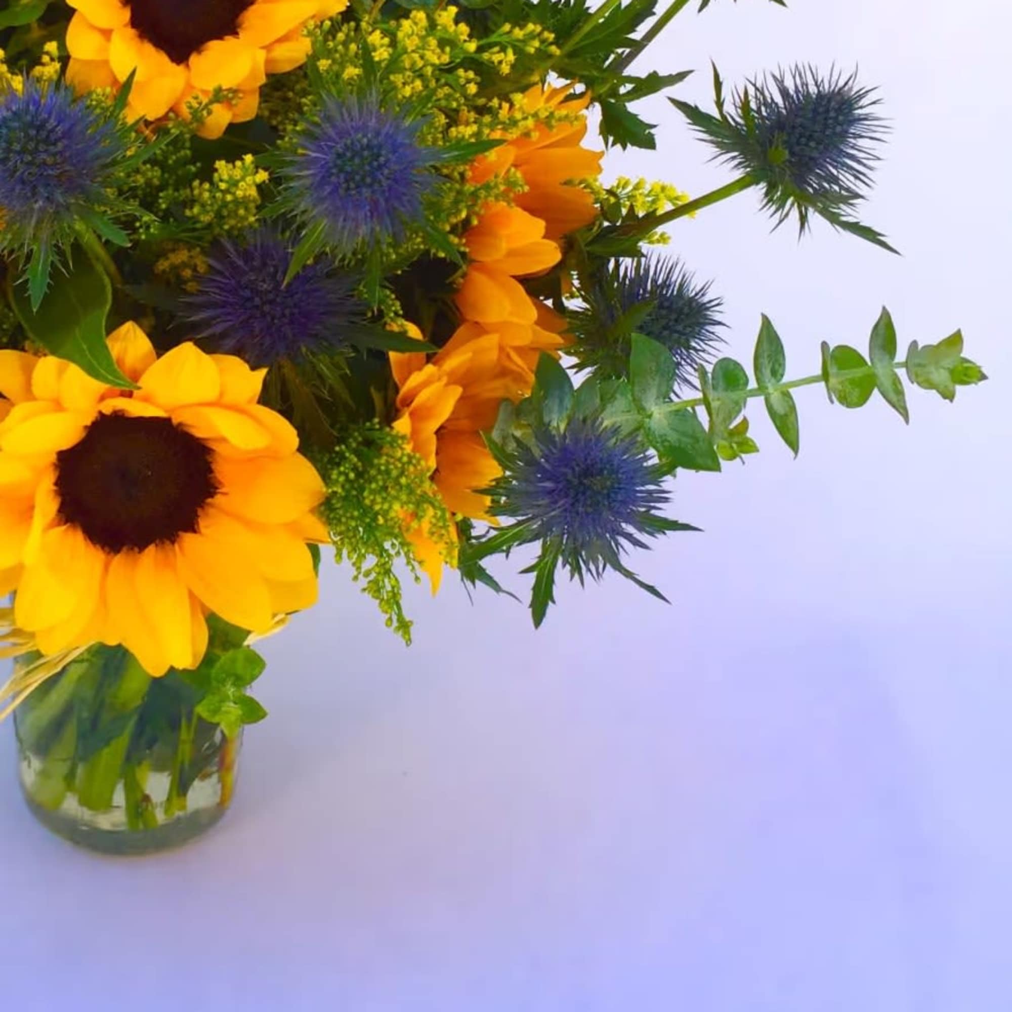 Bouquet of sunflowers and blue thistle in a glass vase