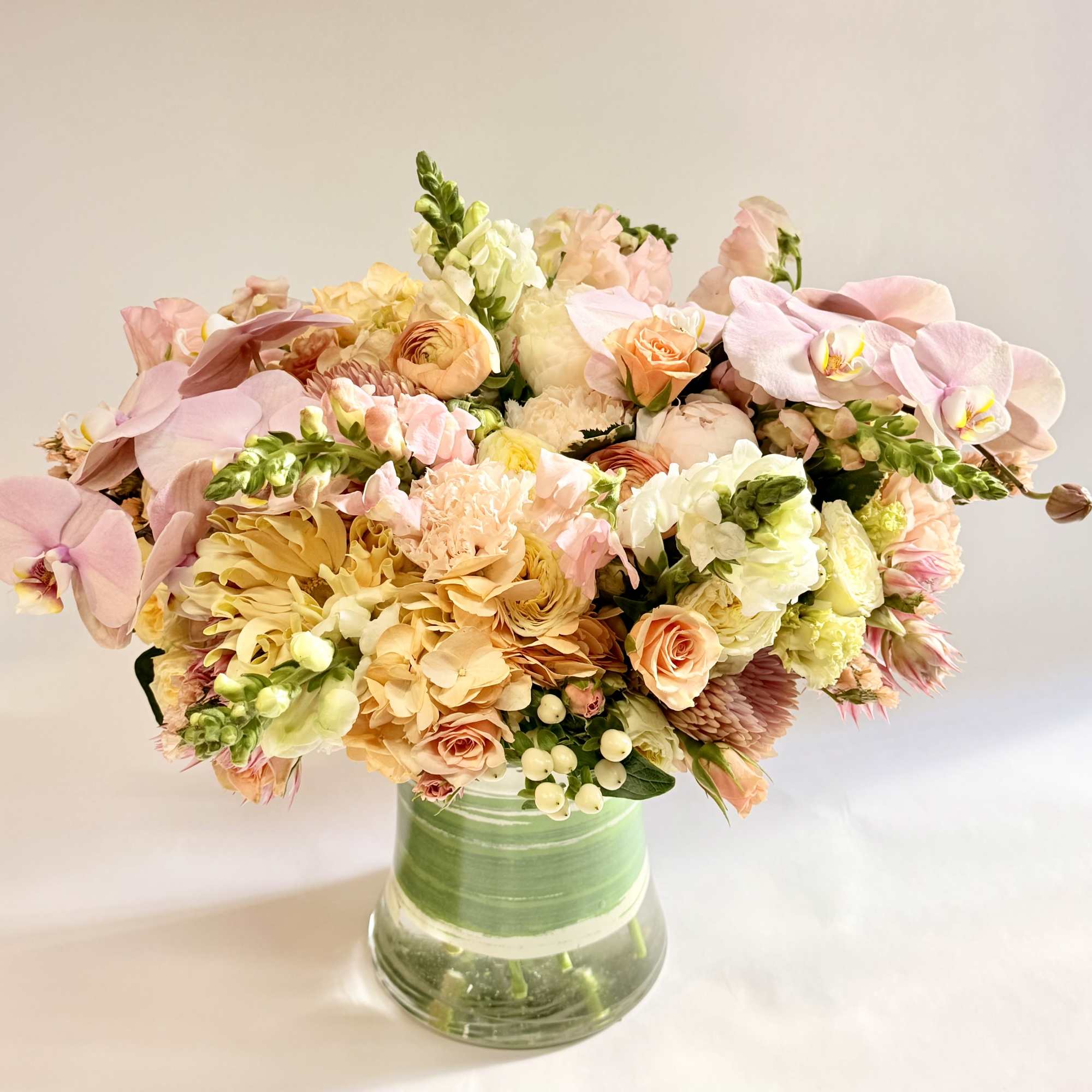 Pastel bouquet of orchids, roses, and mixed blooms in a green glass vase