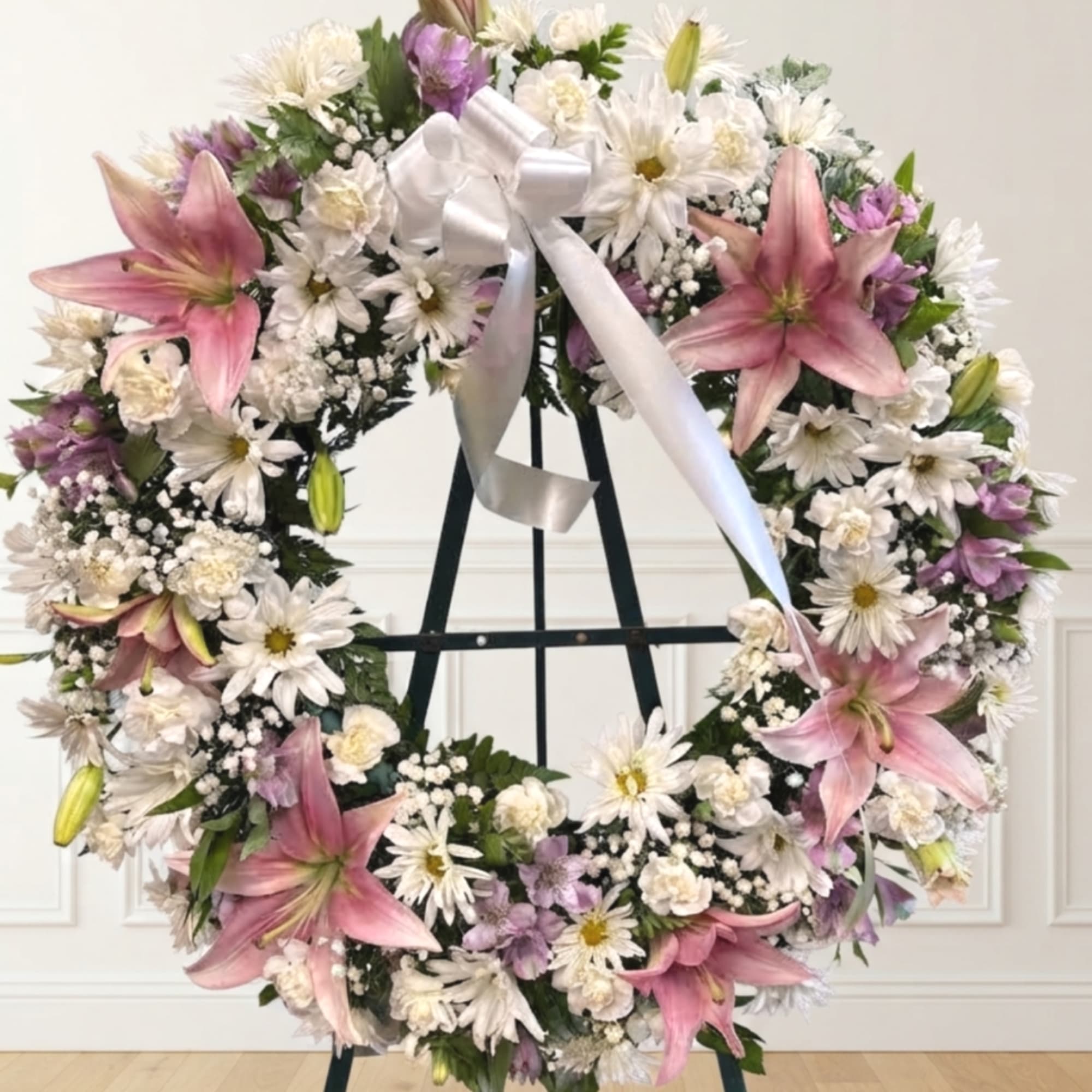 Large floral wreath with pink lilies, white daisies, and a white ribbon on an easel