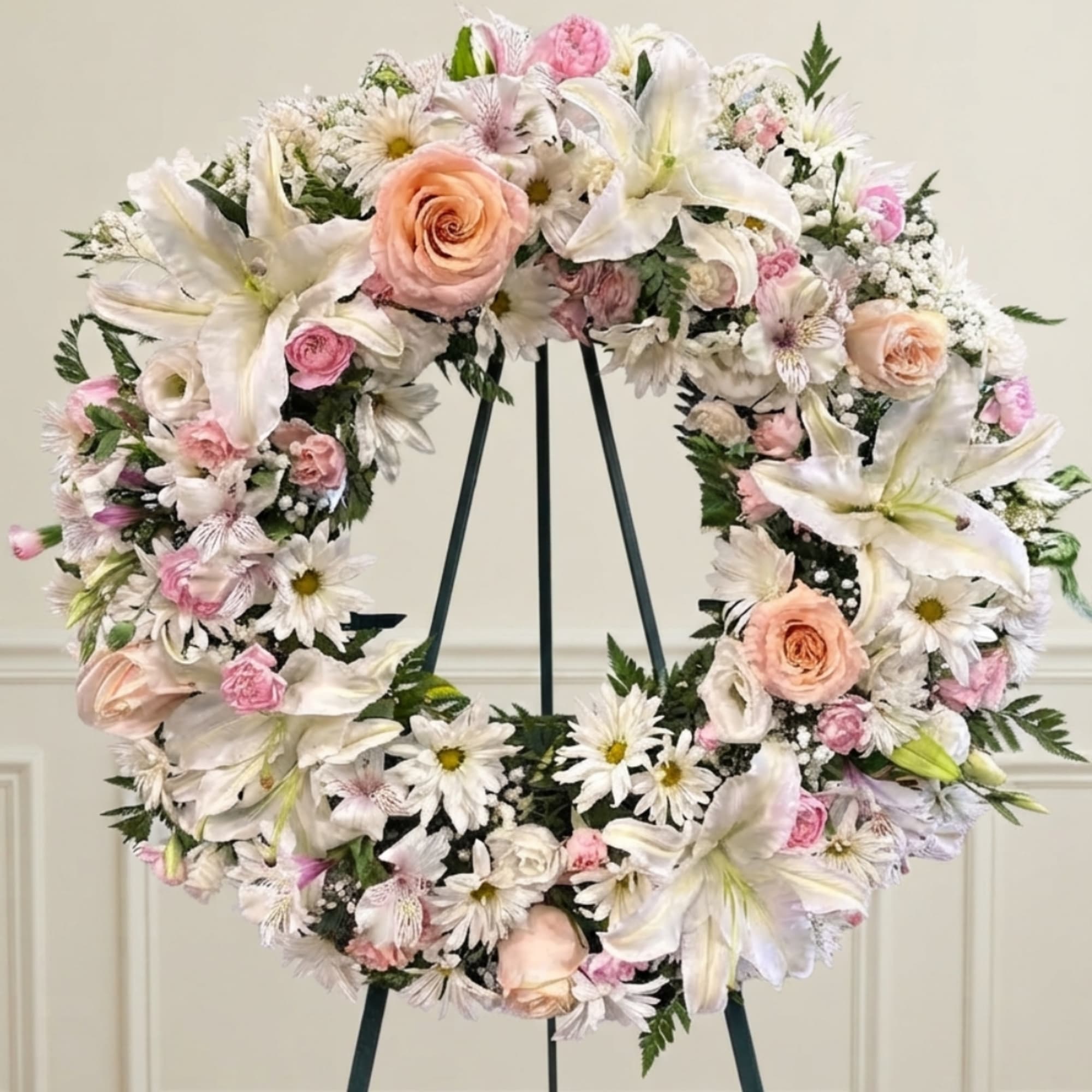 Round floral wreath with white lilies, pink roses, and daisies on a stand