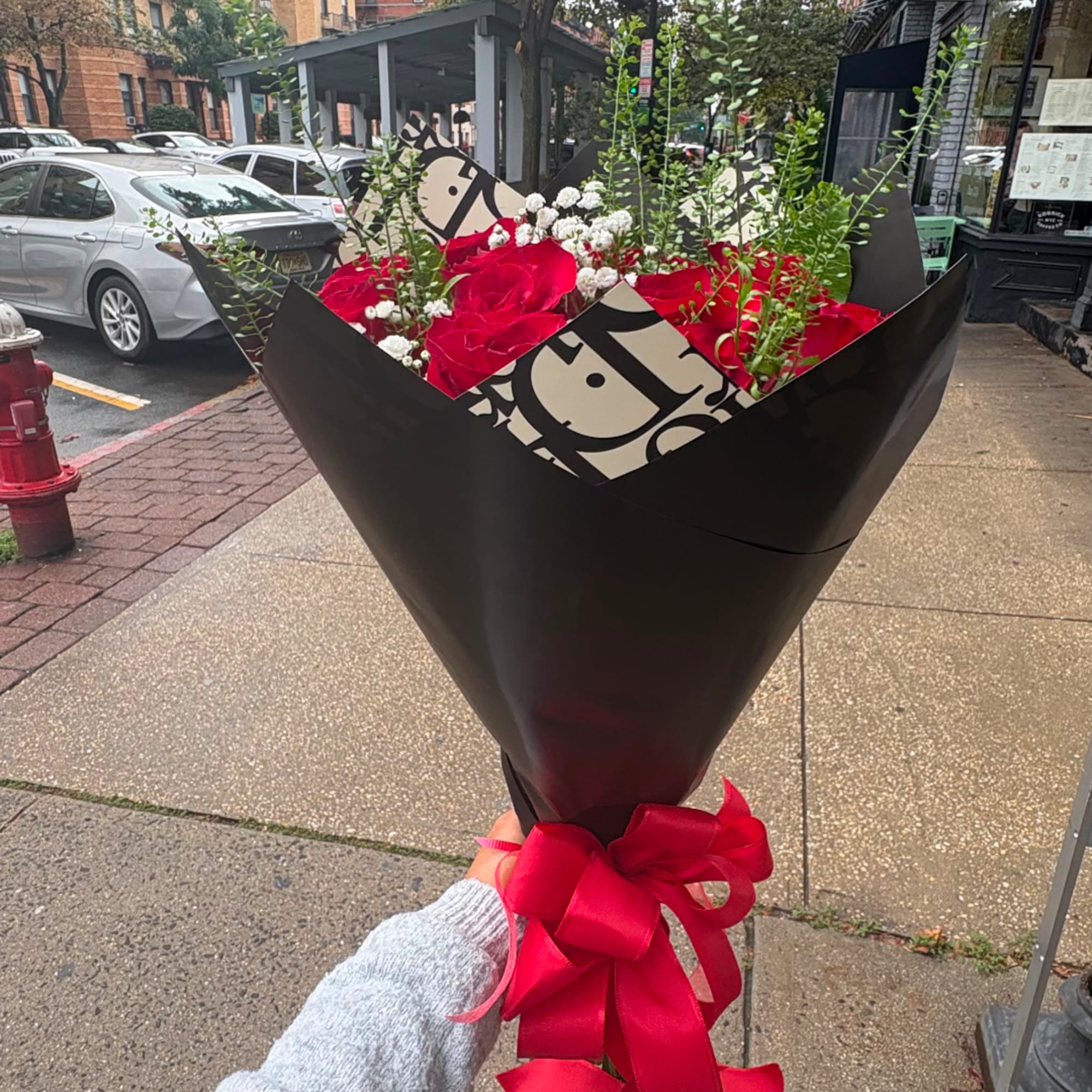 Handheld bouquet of red roses with baby's breath in black wrap