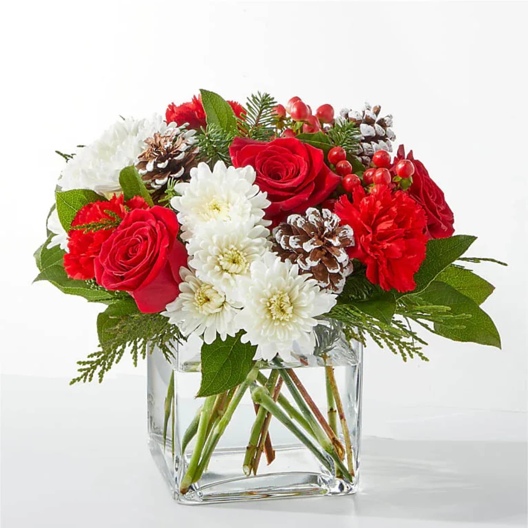 Red roses and white daisies in a clear glass vase with pinecones