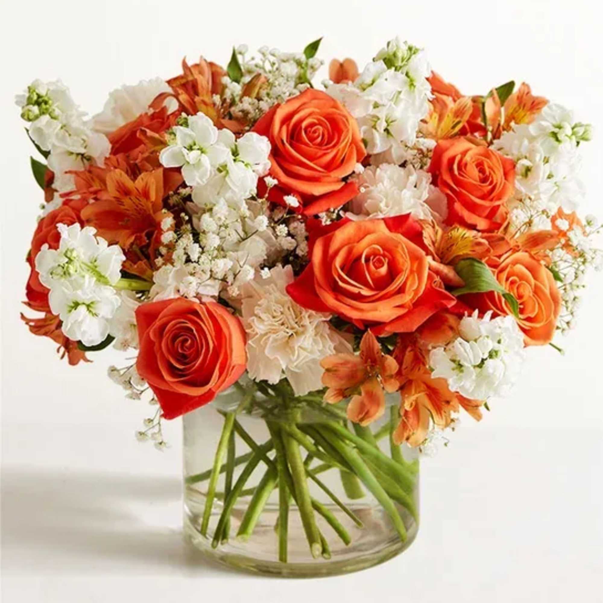 Orange roses and white flowers arranged in a clear glass vase