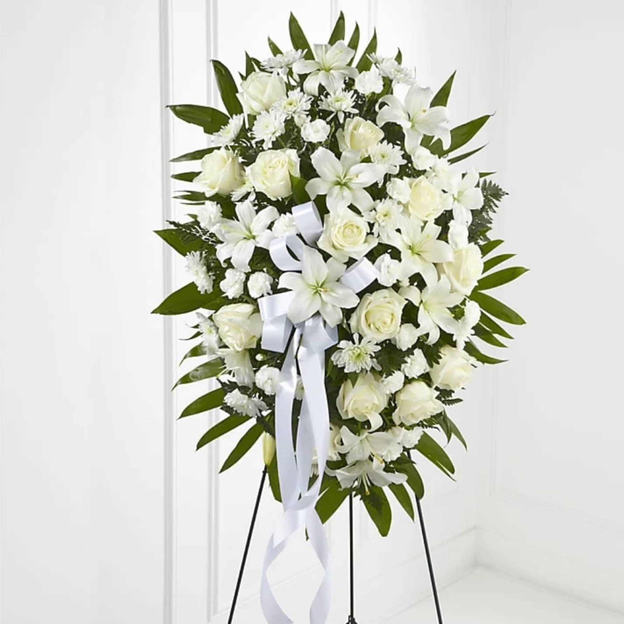 White floral standing spray on an easel with a ribbon bow