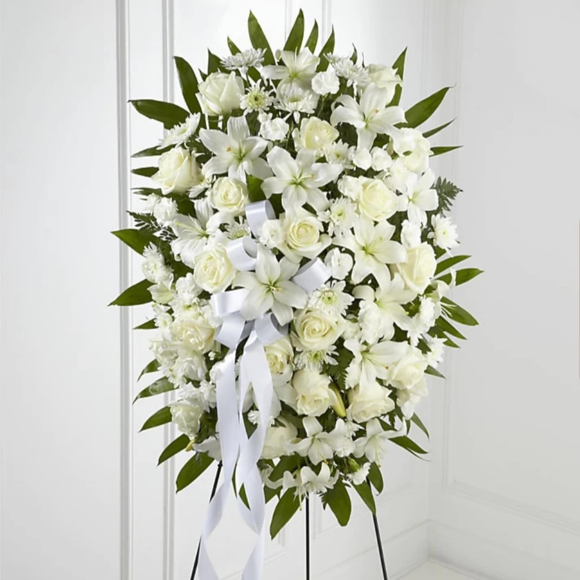 White floral standing spray with roses and lilies on a black easel