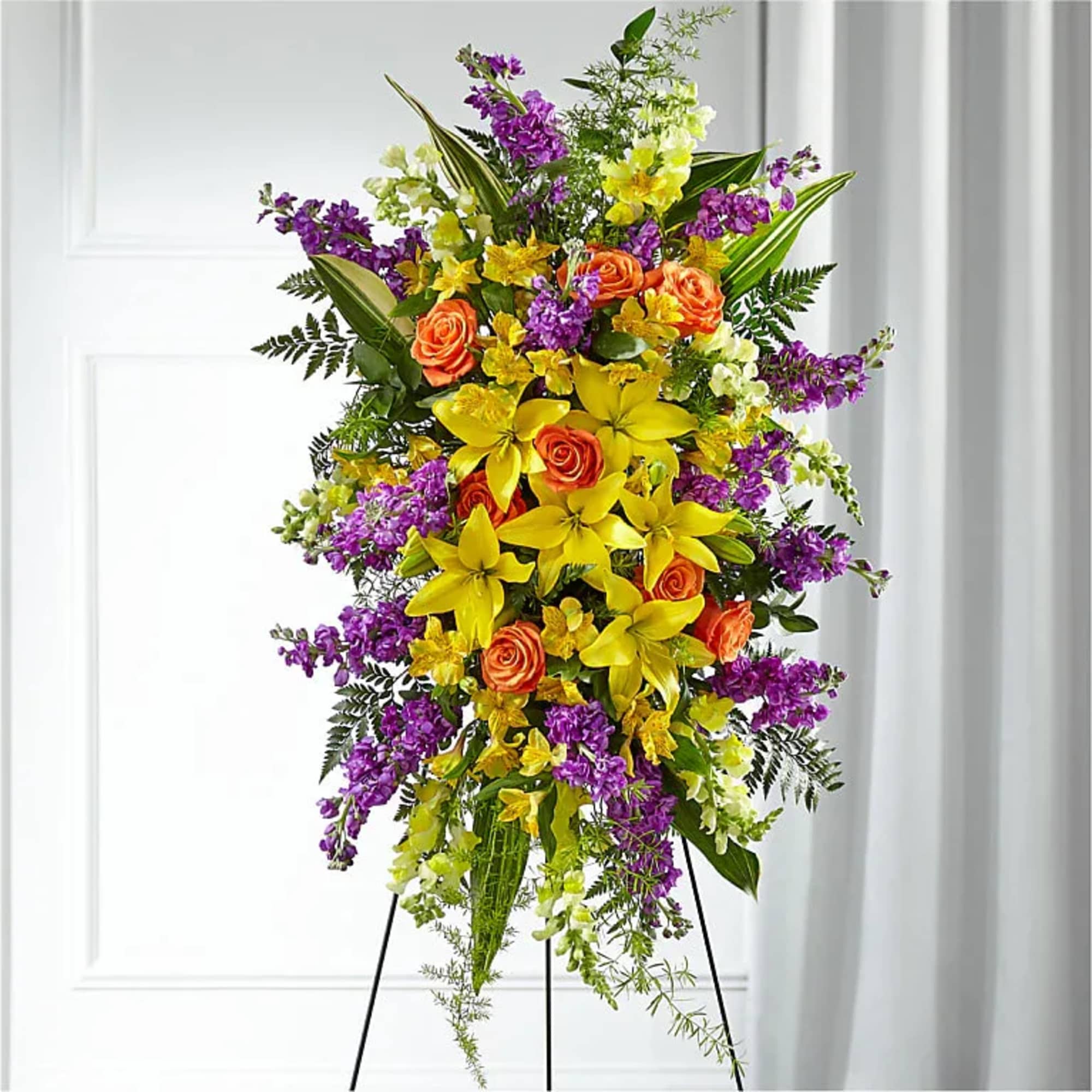 Tall standing floral spray with yellow lilies, orange roses, and purple flowers