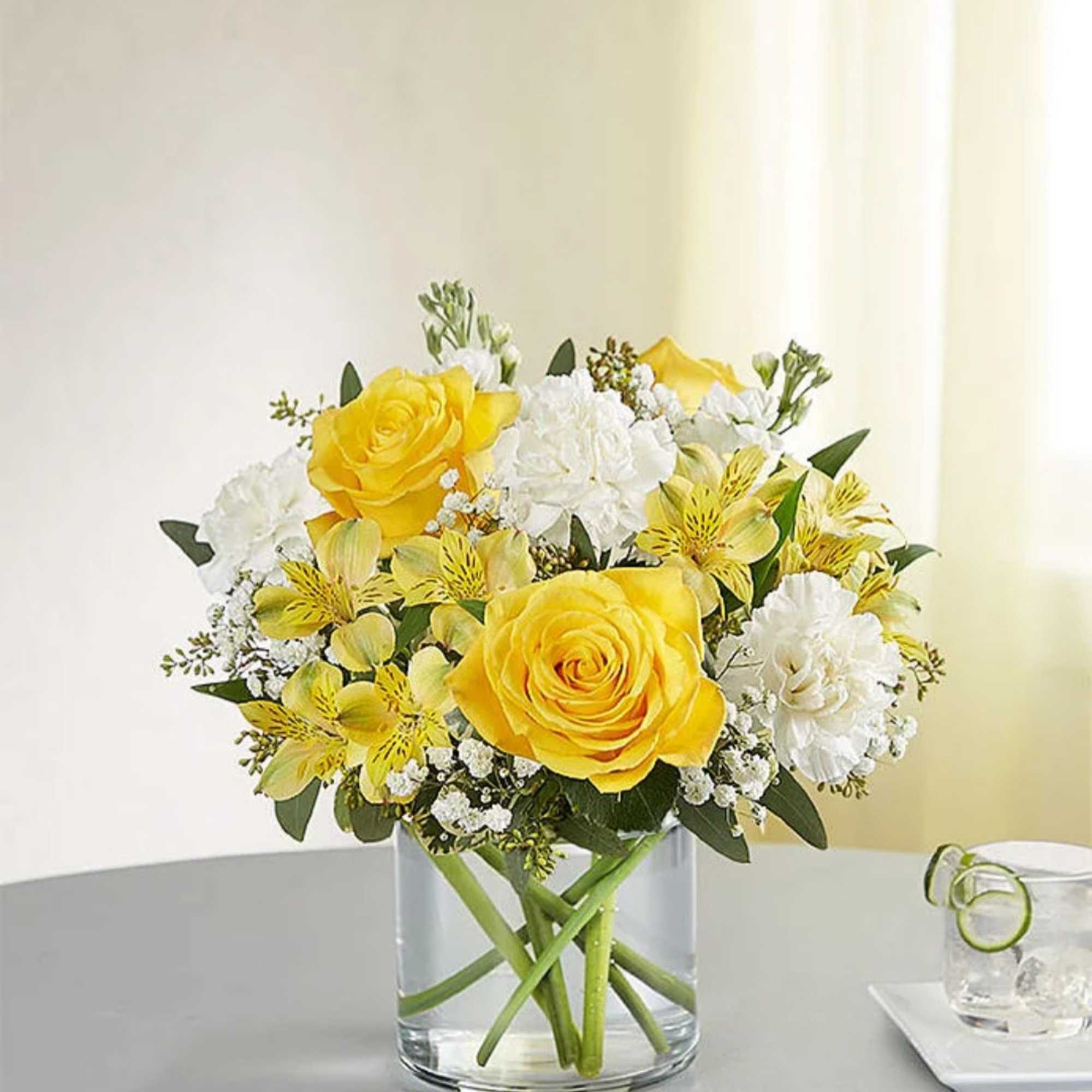 Yellow roses and white flowers in a clear glass vase