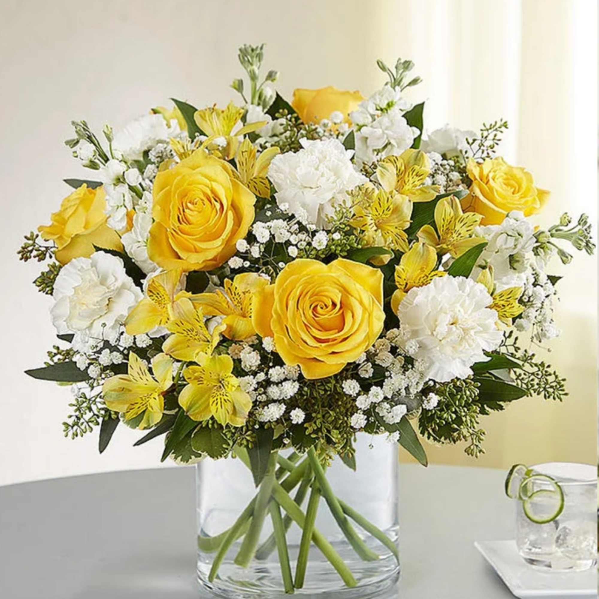 Yellow roses and white flowers in a clear glass vase
