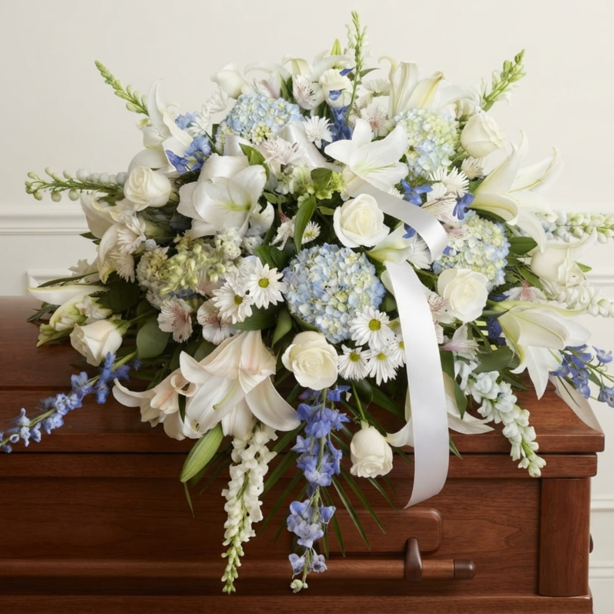 White and blue floral spray on a wooden casket with a white ribbon