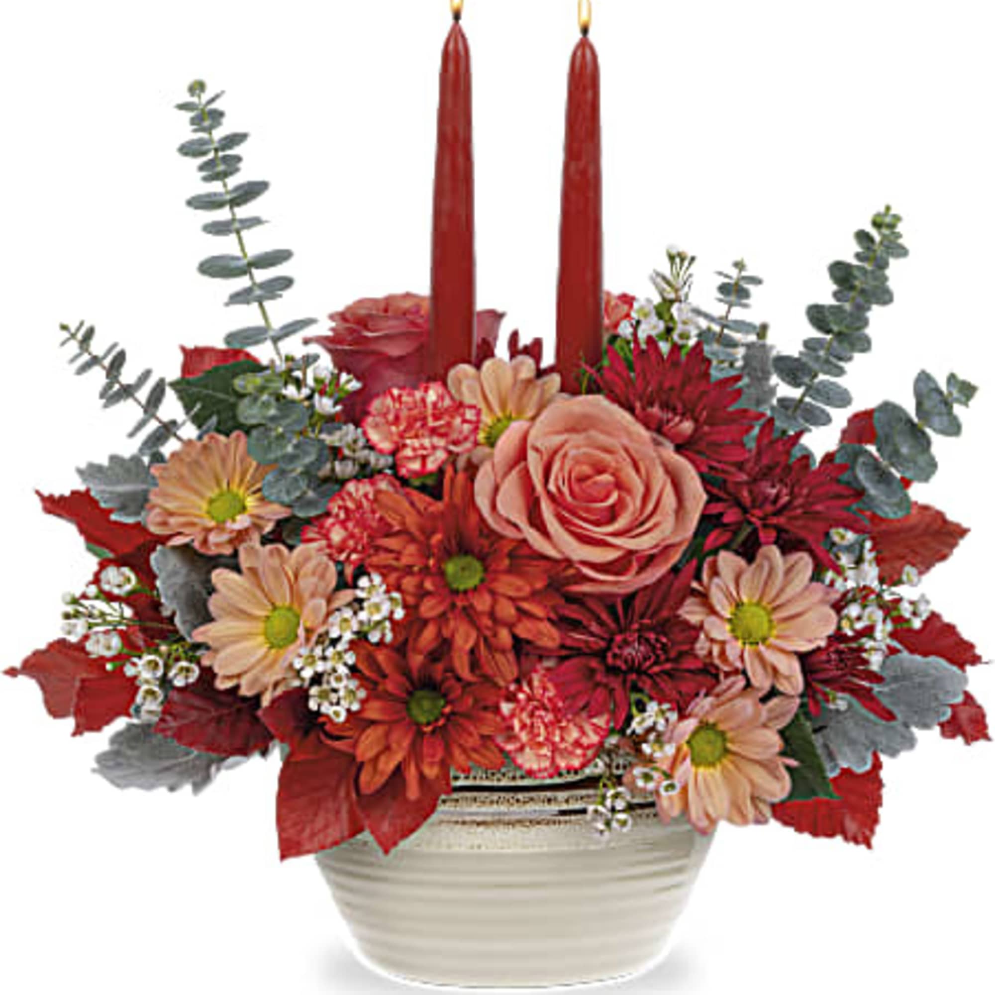 Red and peach floral arrangement with two red taper candles in a white bowl