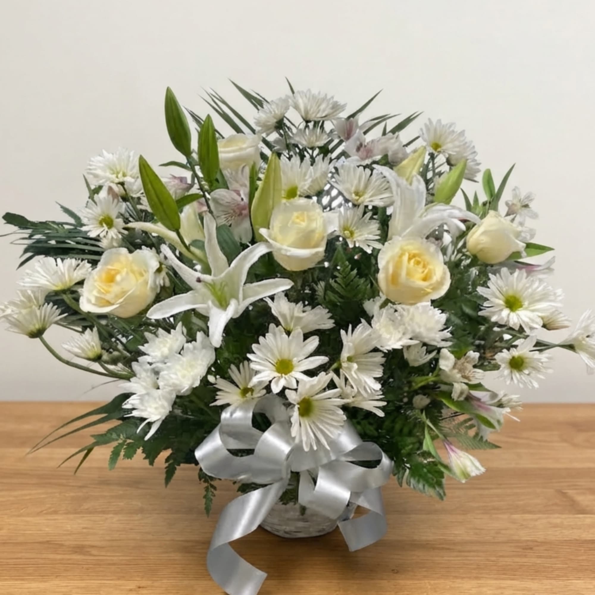 White daisies and cream roses arranged in a basket with a silver ribbon