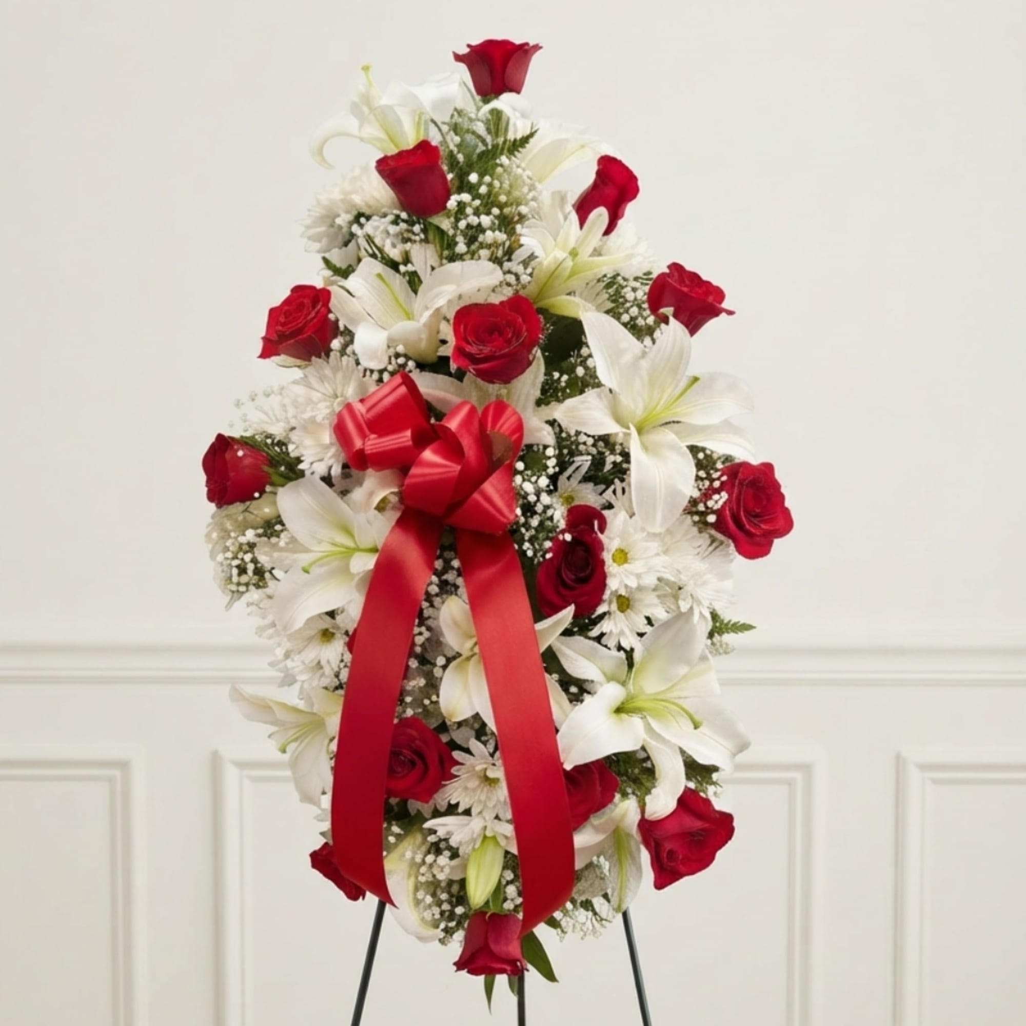 Red roses and white lilies arranged with a red ribbon on a stand