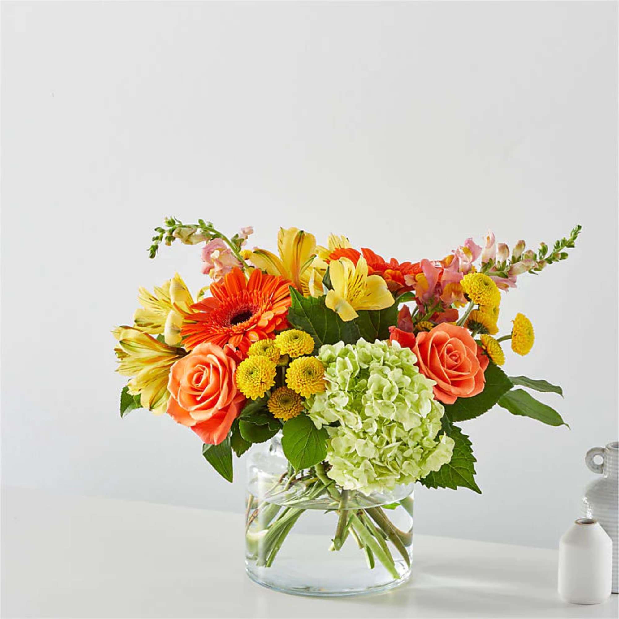 Colorful bouquet of roses, gerbera daisies, hydrangea, and mixed blooms in a glass vase