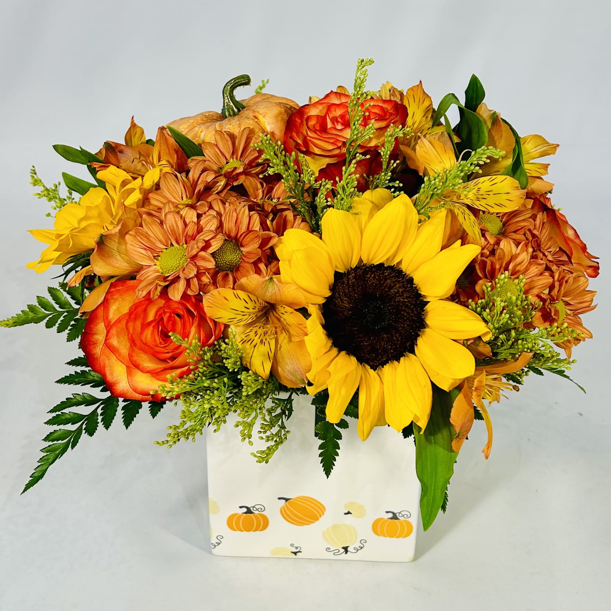 Autumn bouquet of sunflowers, roses, and mums in a pumpkin-decorated box