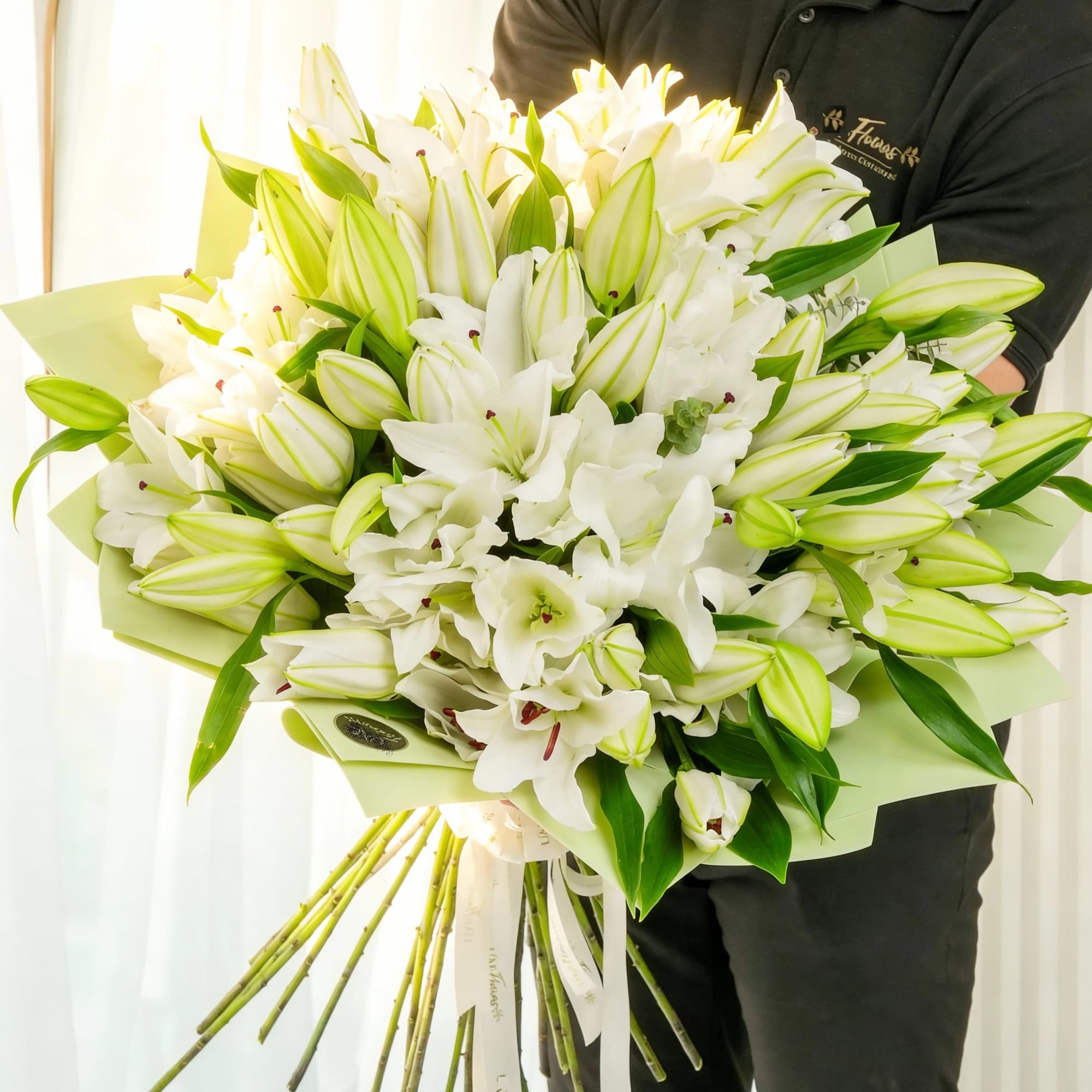 Large bouquet of white lilies and unopened lily buds wrapped in pale green paper