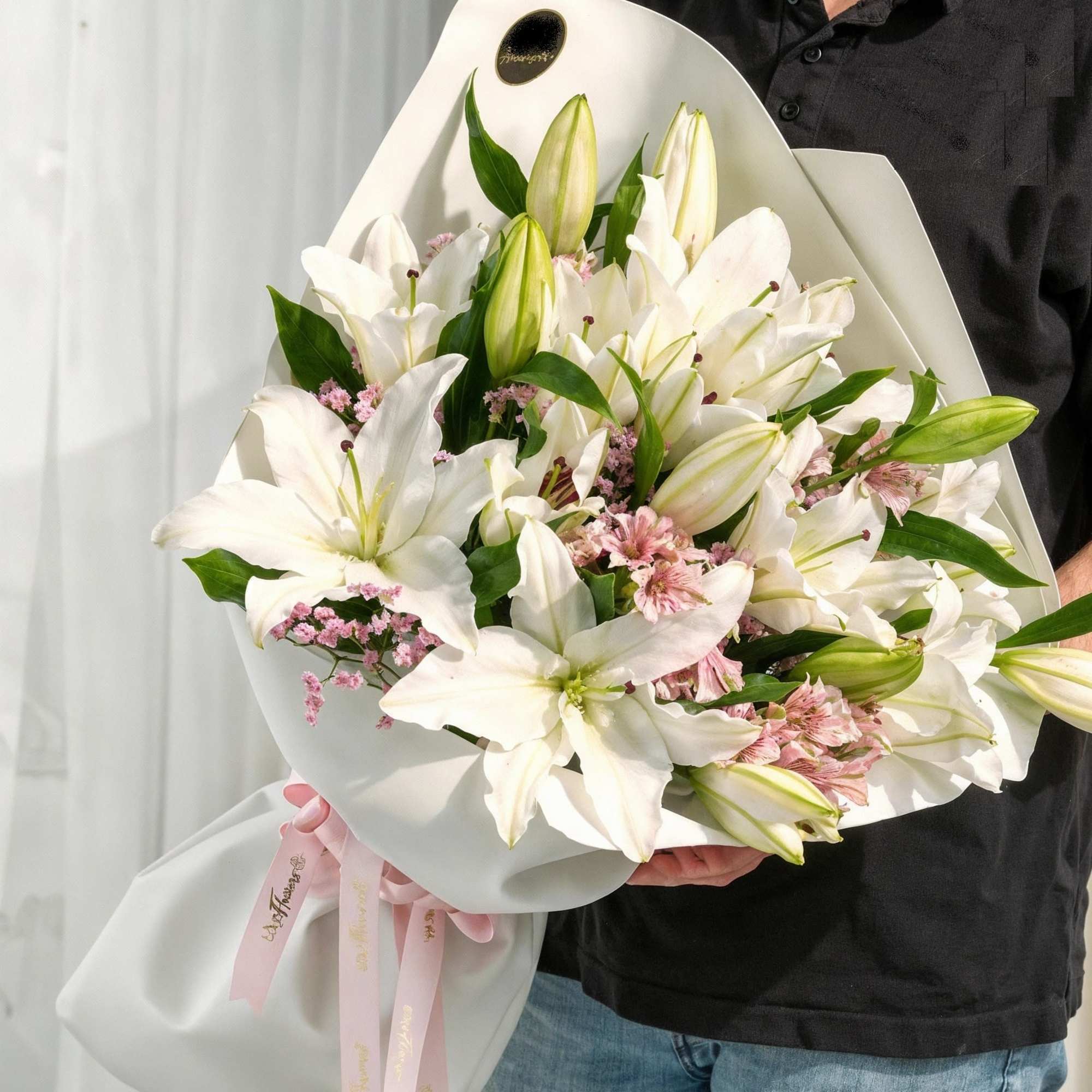 Large bouquet of white lilies with pink filler flowers wrapped in white paper