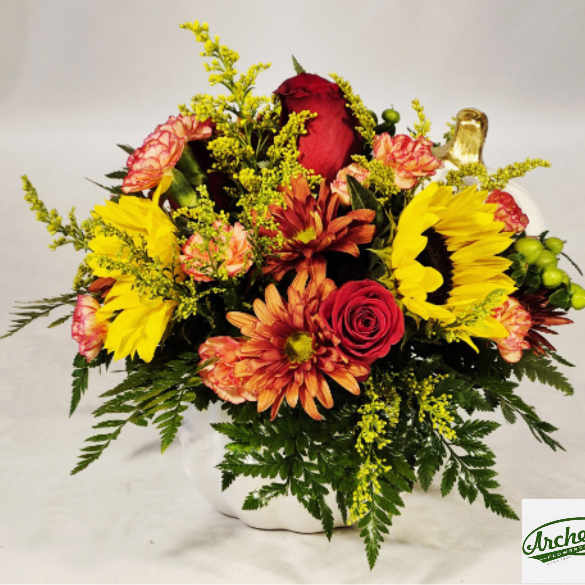Mixed bouquet with red roses, sunflowers, and orange mums in a white vase