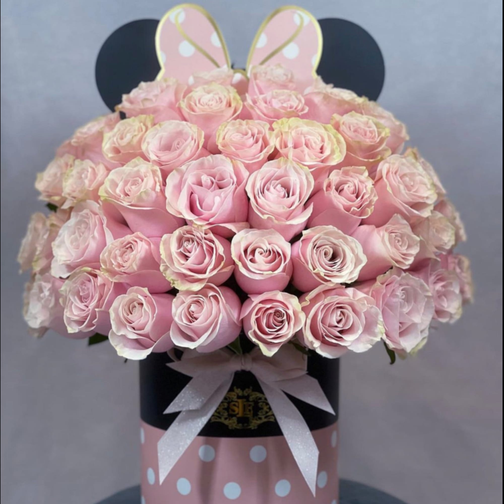 Pink roses arranged in a polka-dot hat box with a ribbon and bunny ears