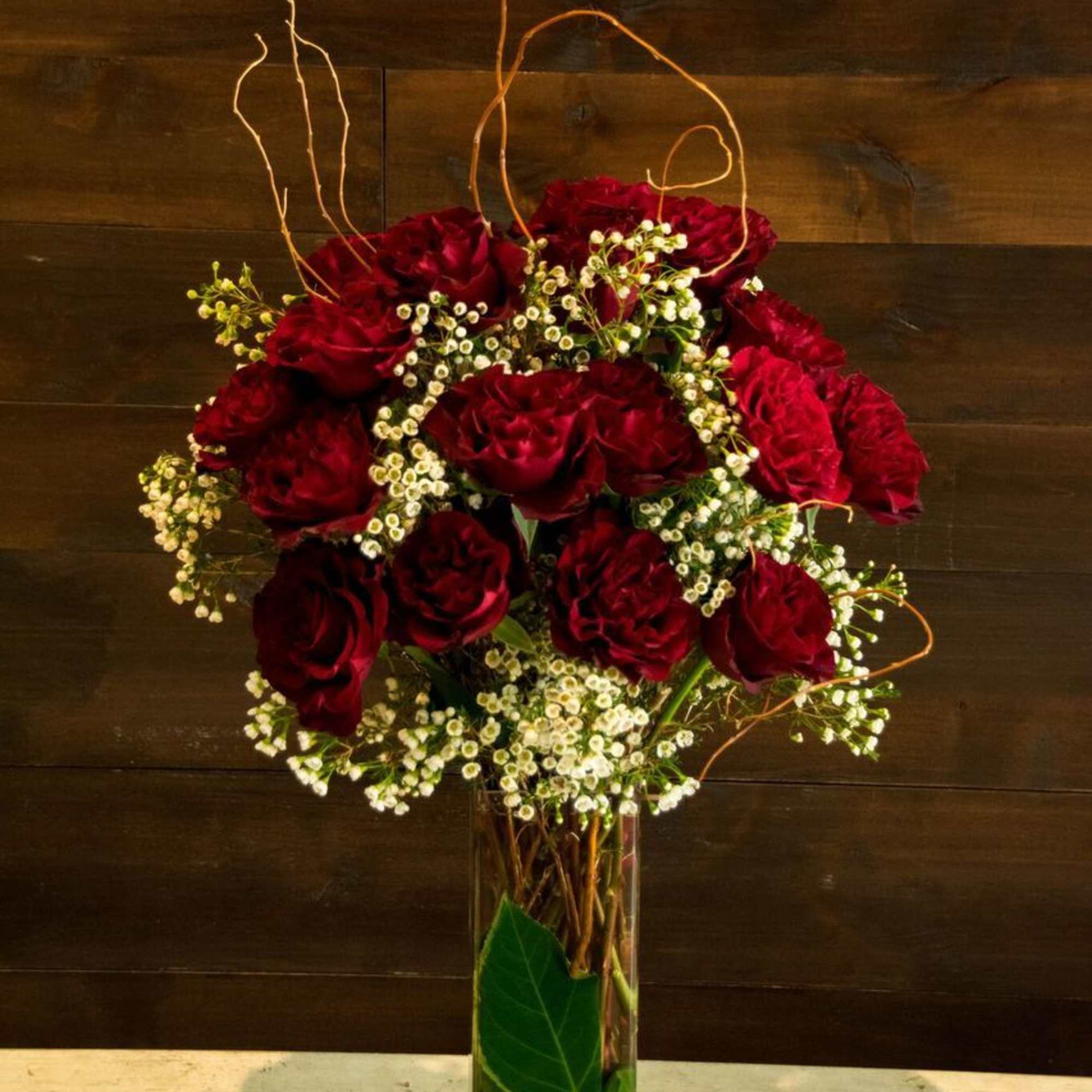 Red roses arranged in a tall glass vase with white filler flowers