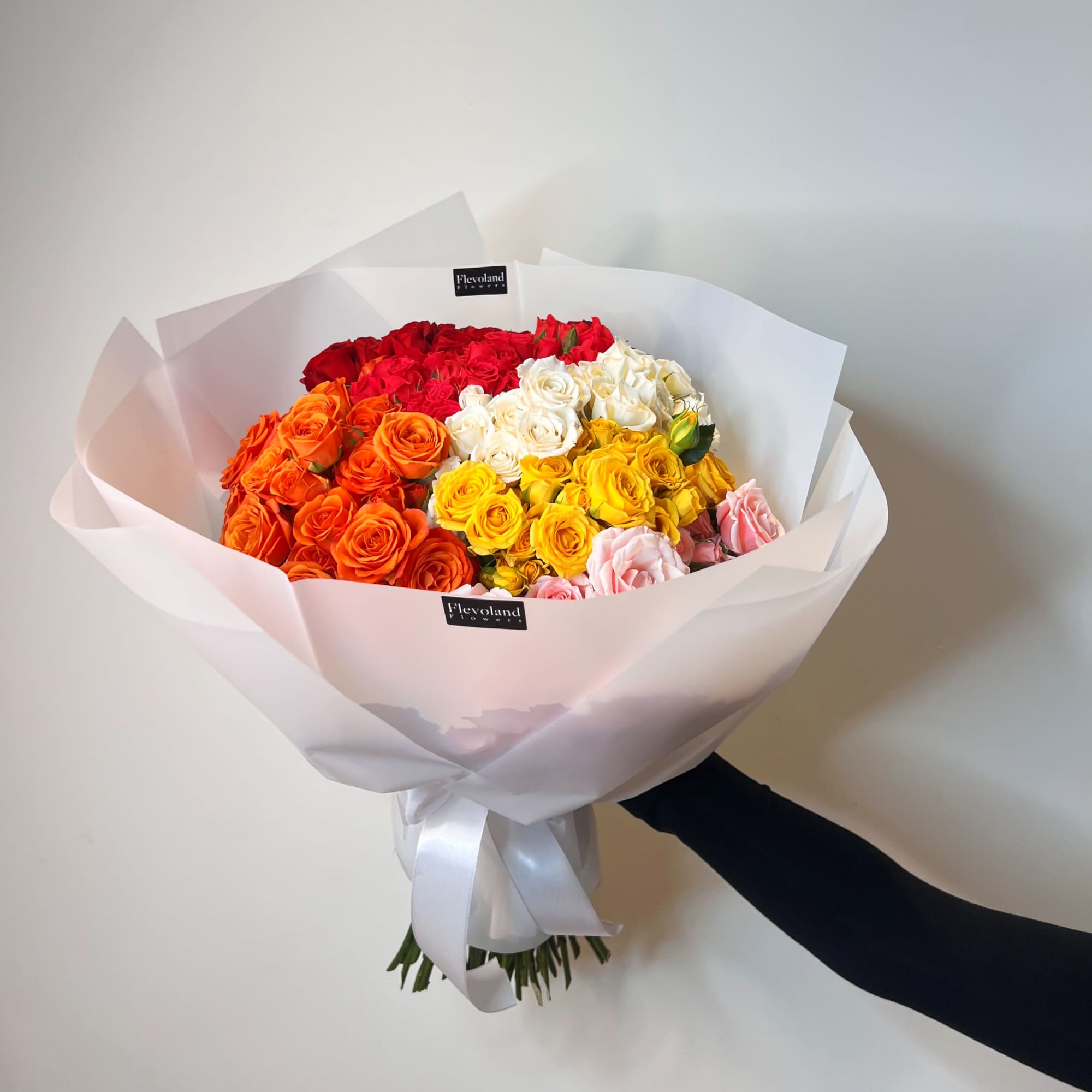 Bouquet of multicolored roses wrapped in white paper with a satin ribbon