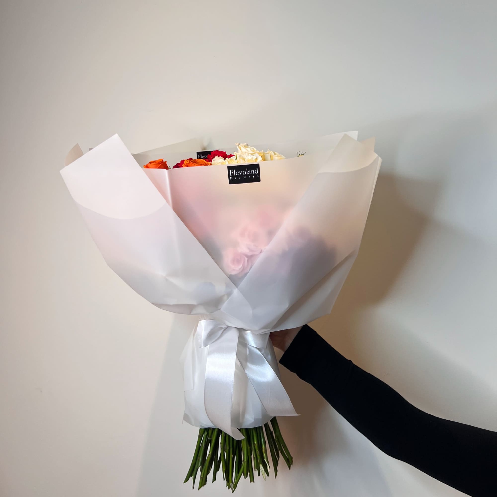 Wrapped bouquet of orange, red, and white roses tied with a white ribbon