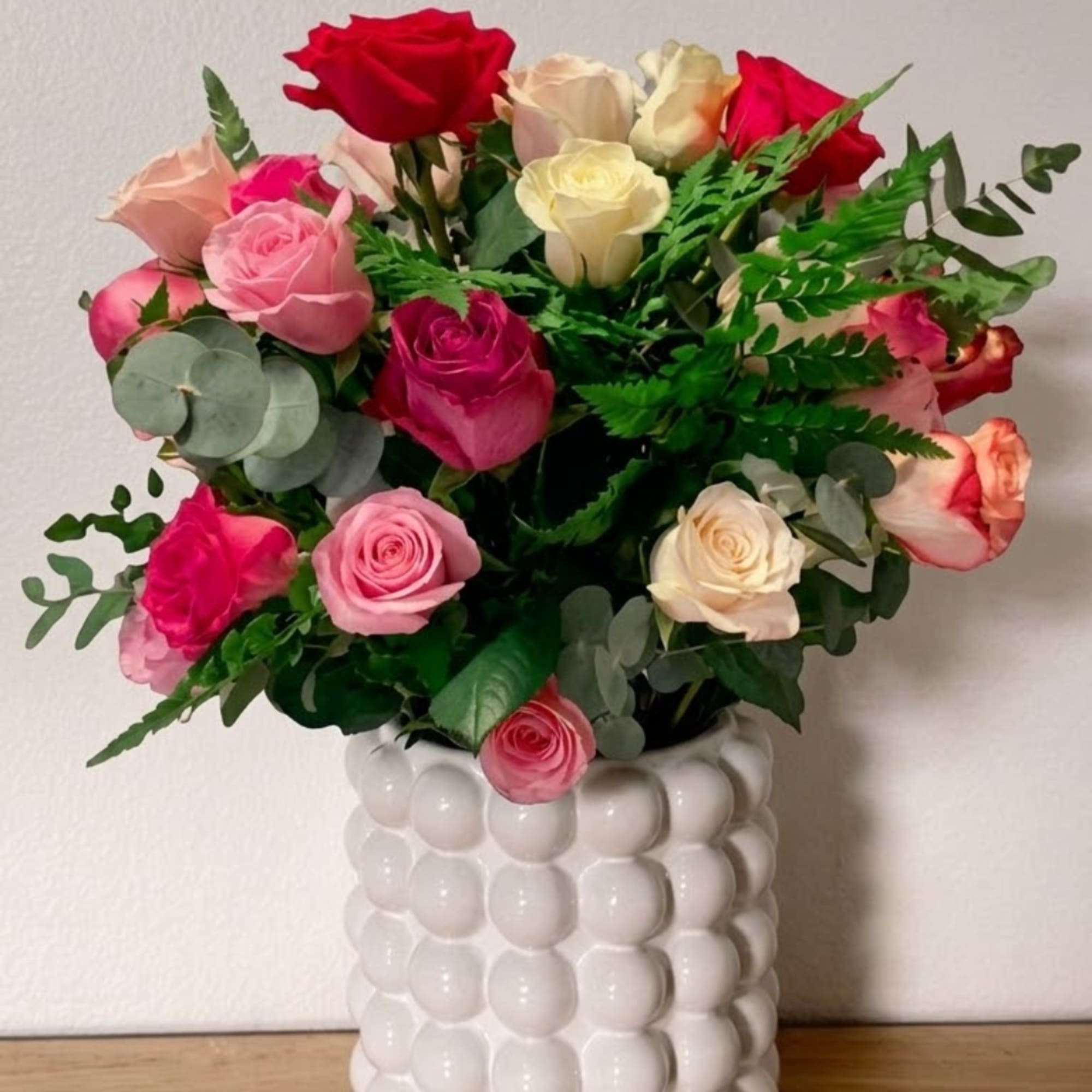 Mixed roses in pink, red, cream, and peach in a white vase