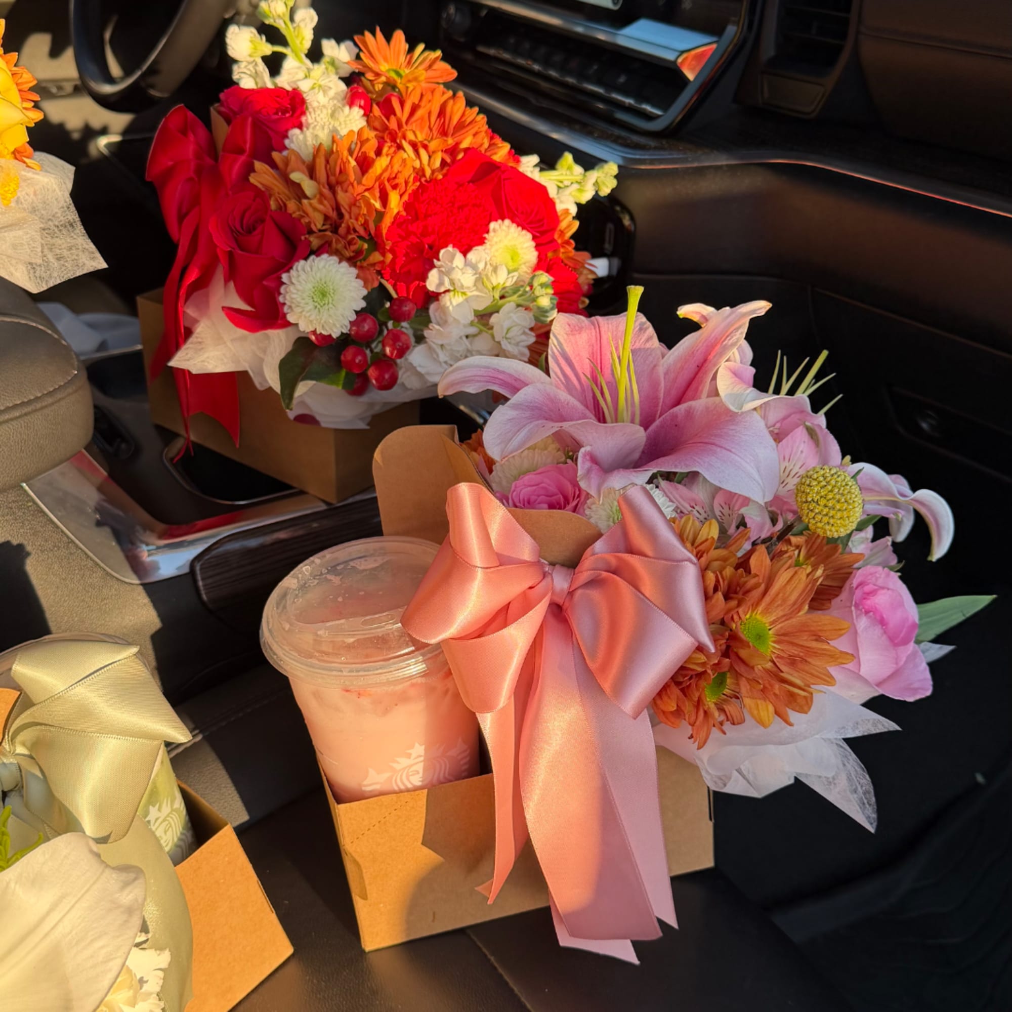 Two mixed flower bouquets with ribbons and a drink cup in a car seat