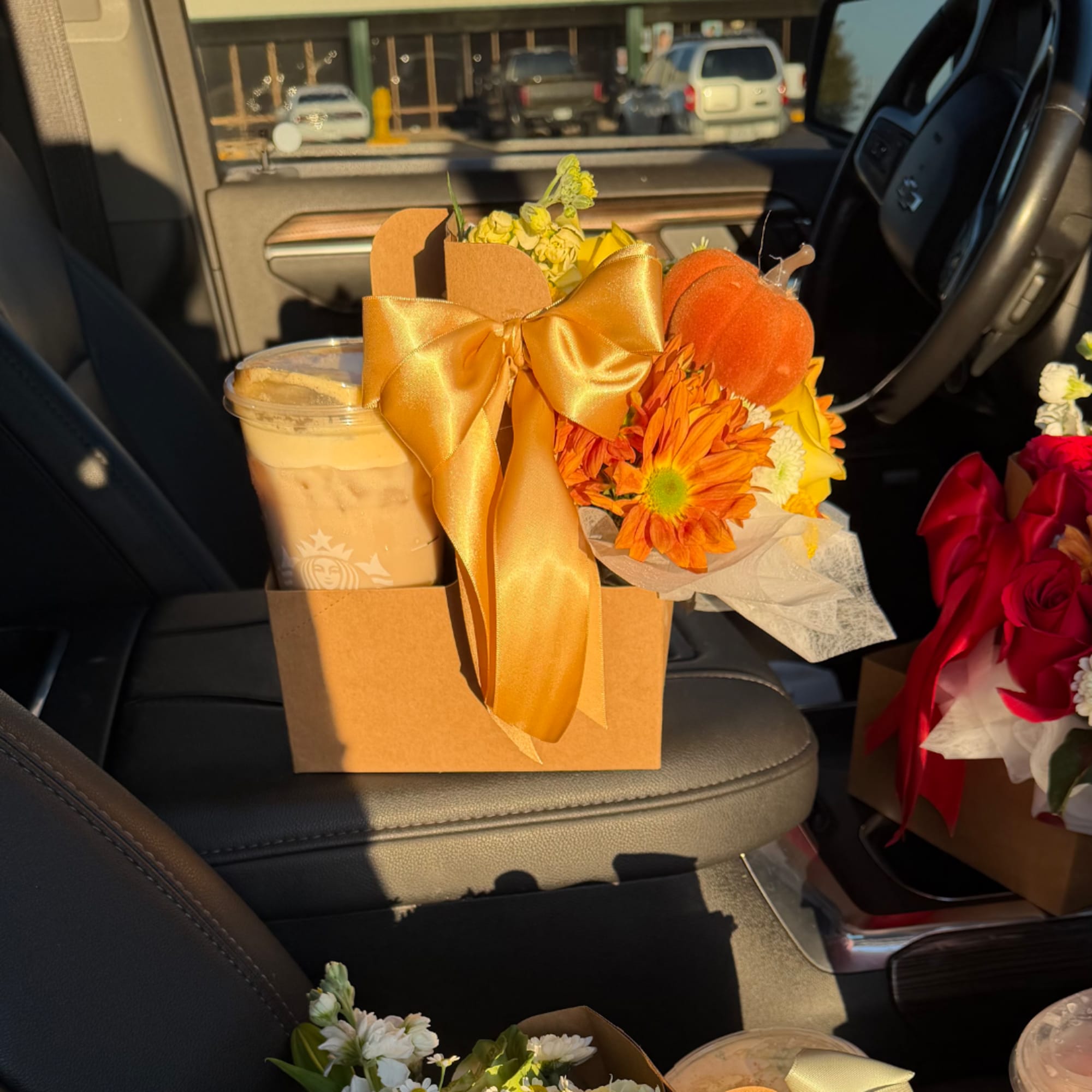Orange flower gift box with a gold bow and iced drink in a car seat