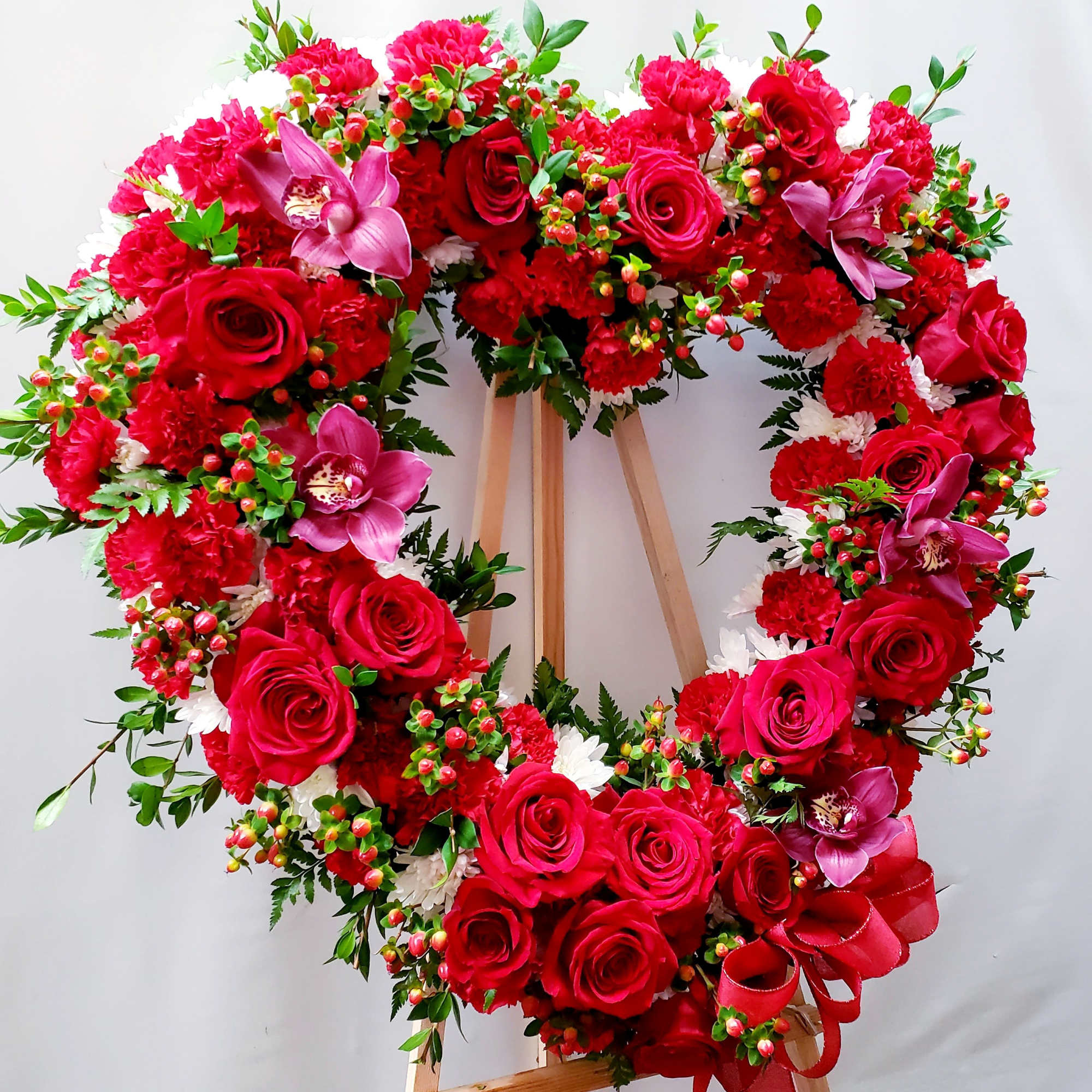 Heart-shaped floral wreath with red roses and pink orchids on a stand