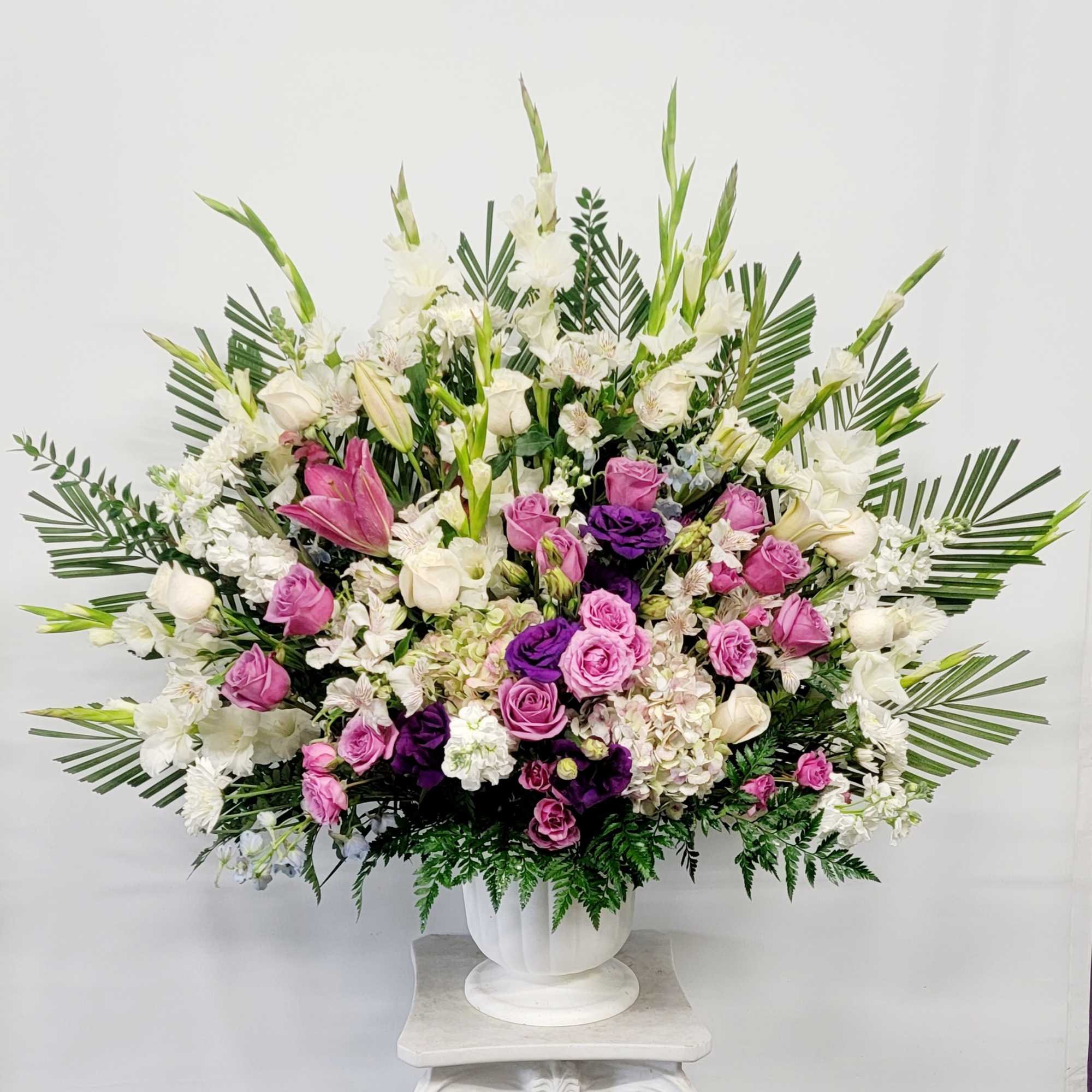 Large white, pink, and purple floral arrangement in a white urn vase