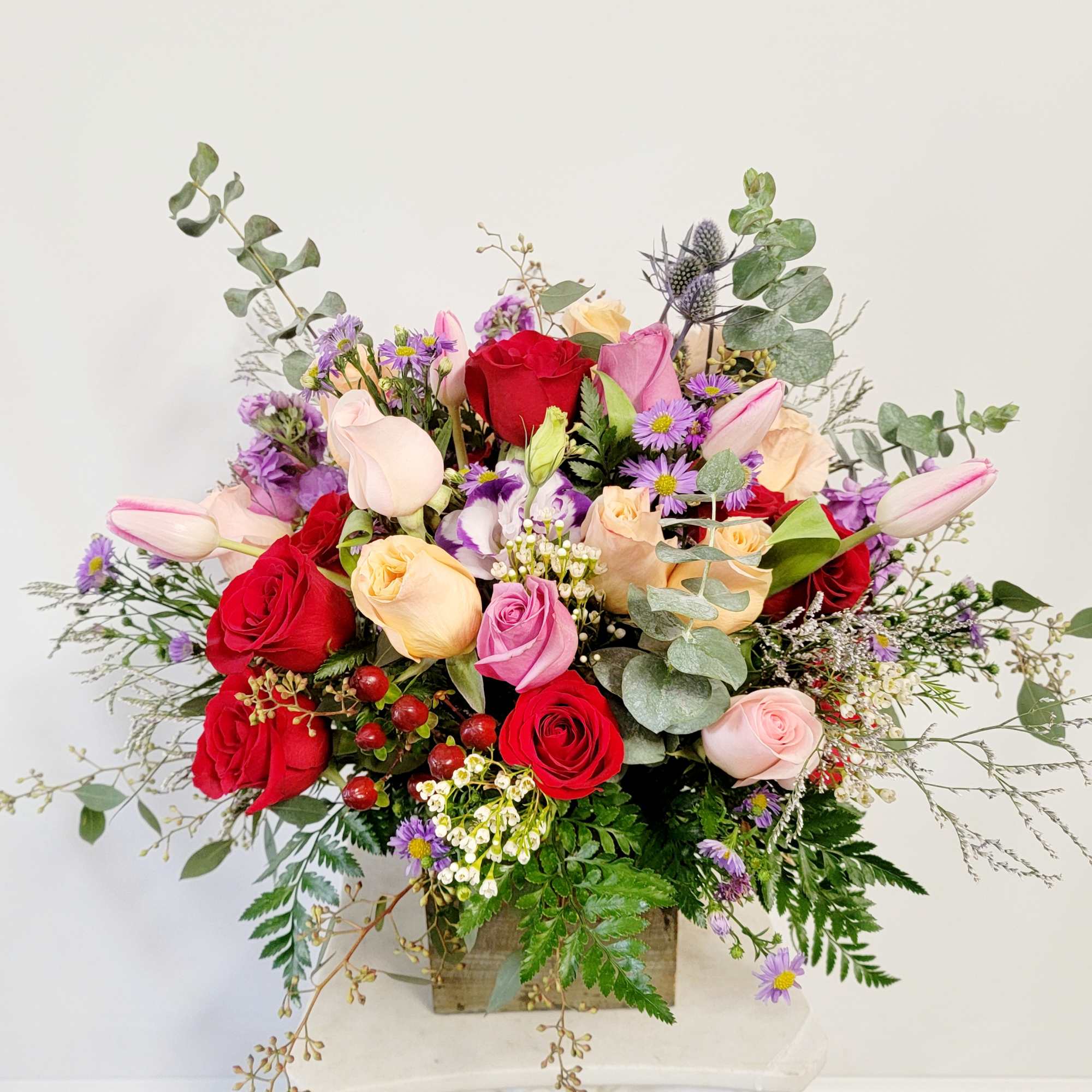 Mixed bouquet of red, pink, and cream roses with purple daisies in a wooden box