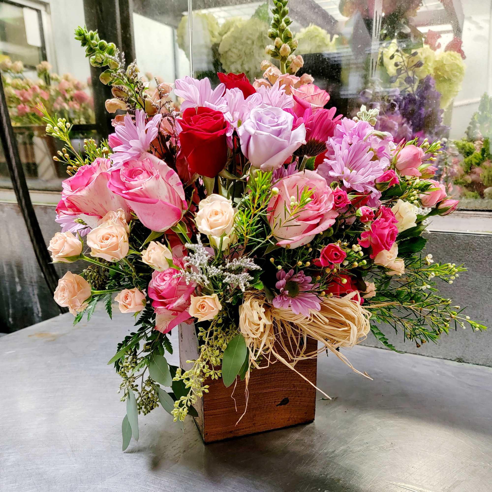 Mixed pink and red flower arrangement in a wooden box