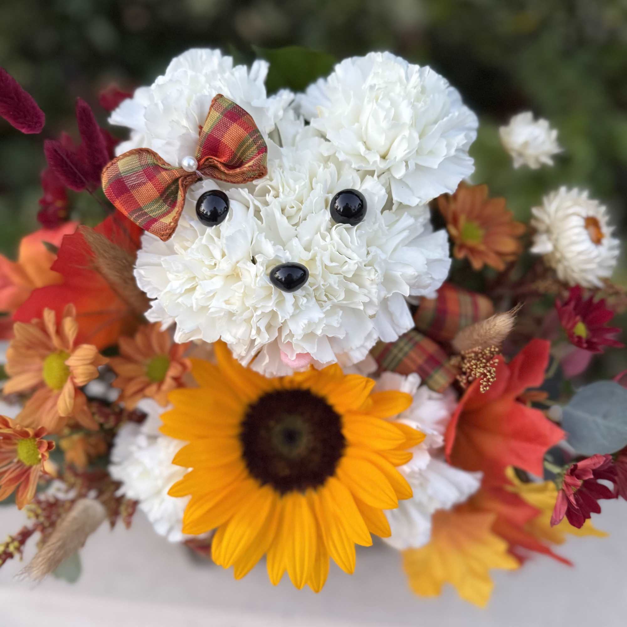White flower arrangement shaped like a bear with a plaid bow and sunflower accent
