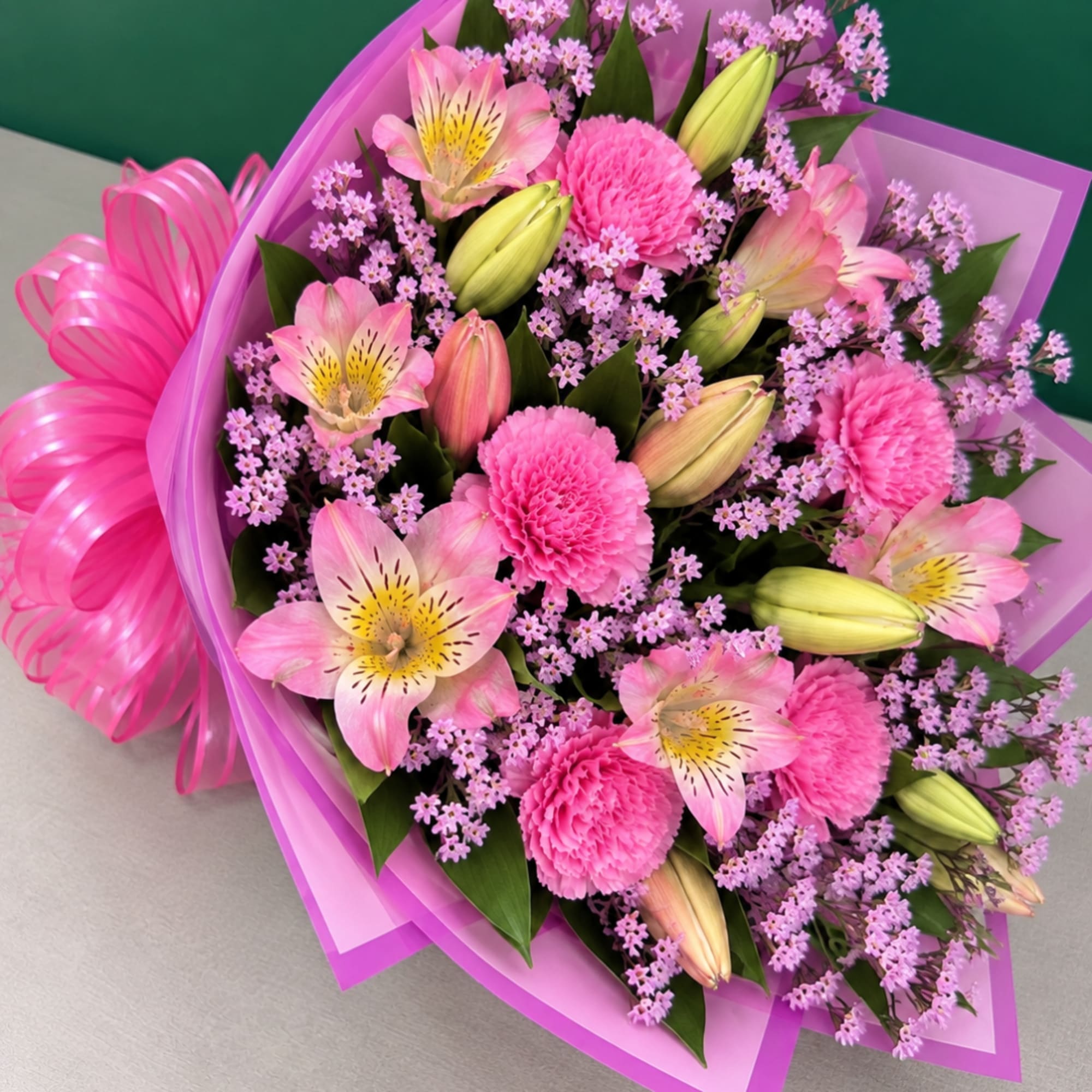 Pink bouquet with lilies, carnations, and purple filler flowers wrapped in pink paper