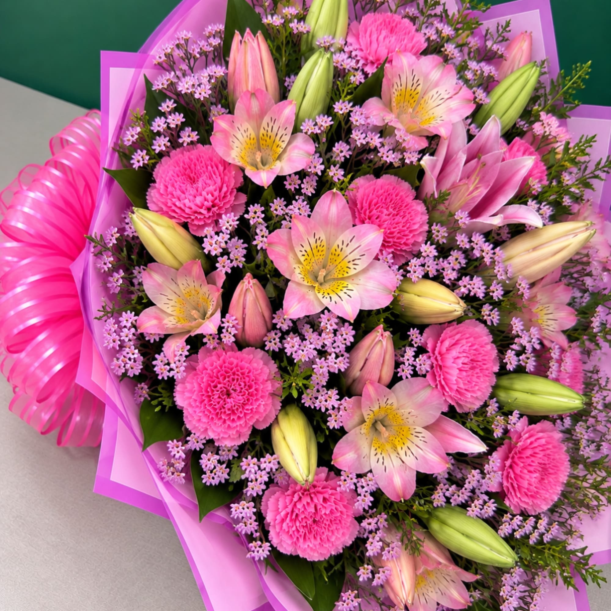 Pink bouquet with lilies, carnations, and small purple filler flowers